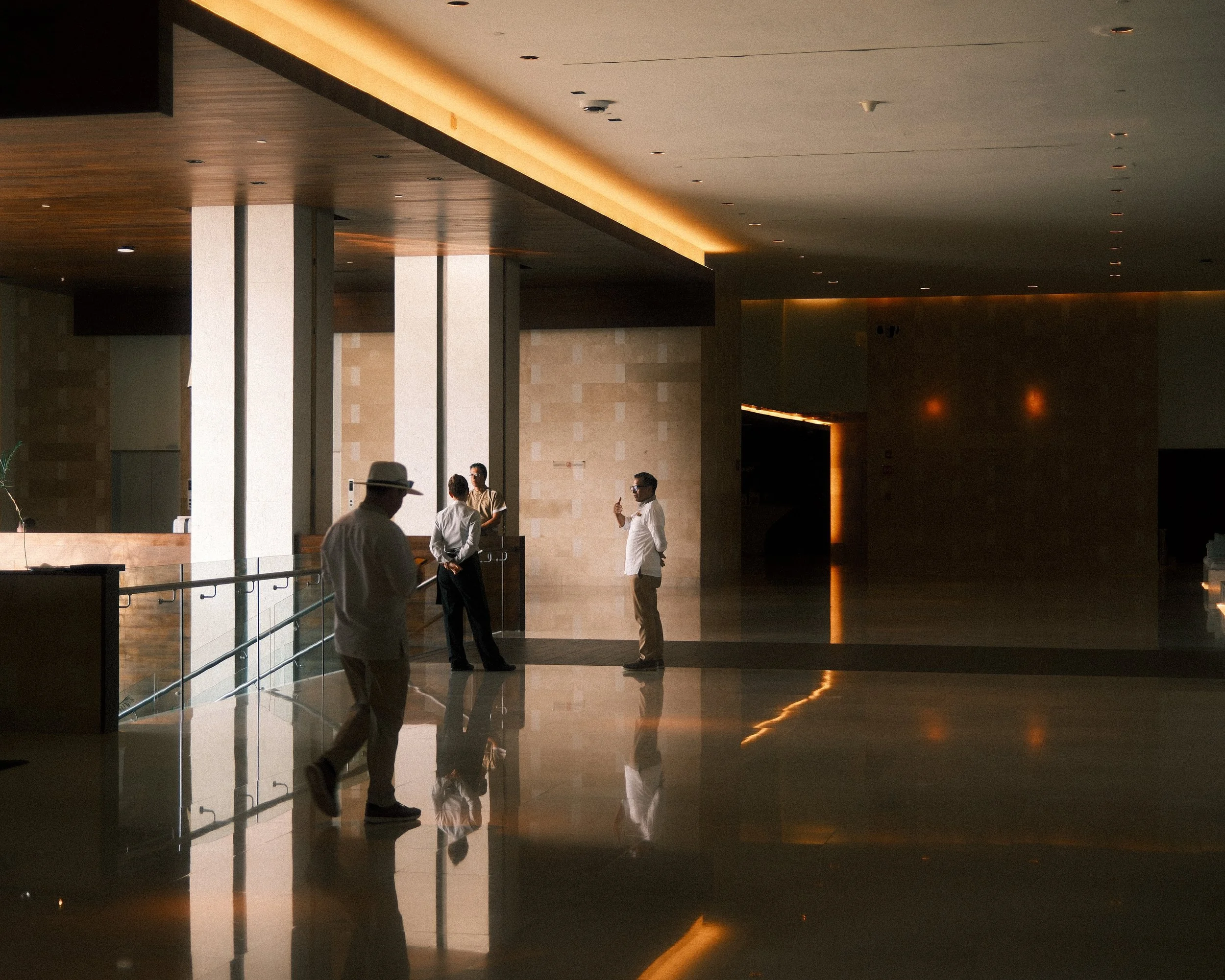 Interior of a modern building lobby with four people, three men and one woman, engaging in conversation or walking.