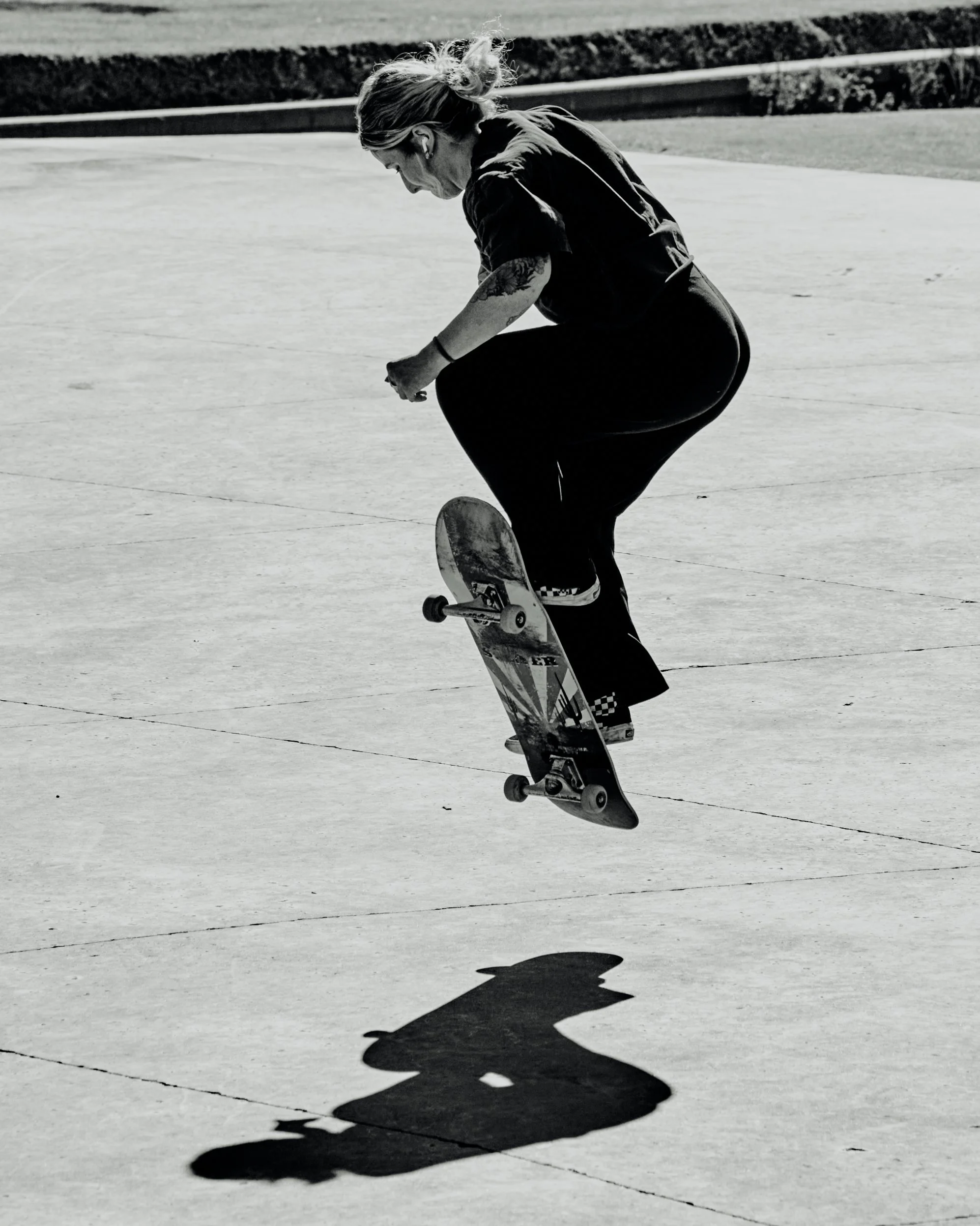 A woman performing a skateboarding trick on a concrete surface, casting a shadow.