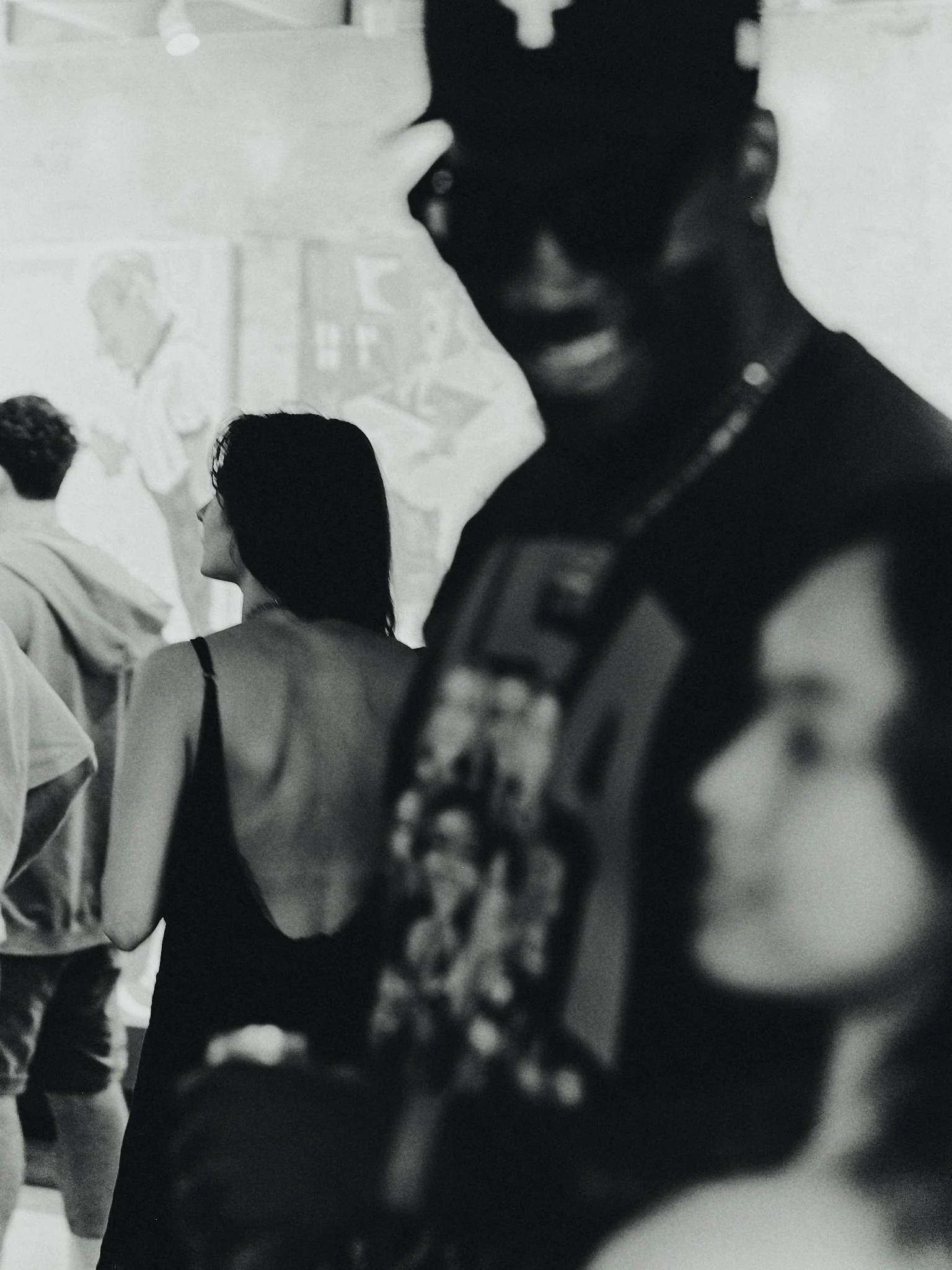 Black and white photo of several people, one in the foreground holding a camera and another in the background walking with a woman and other individuals.