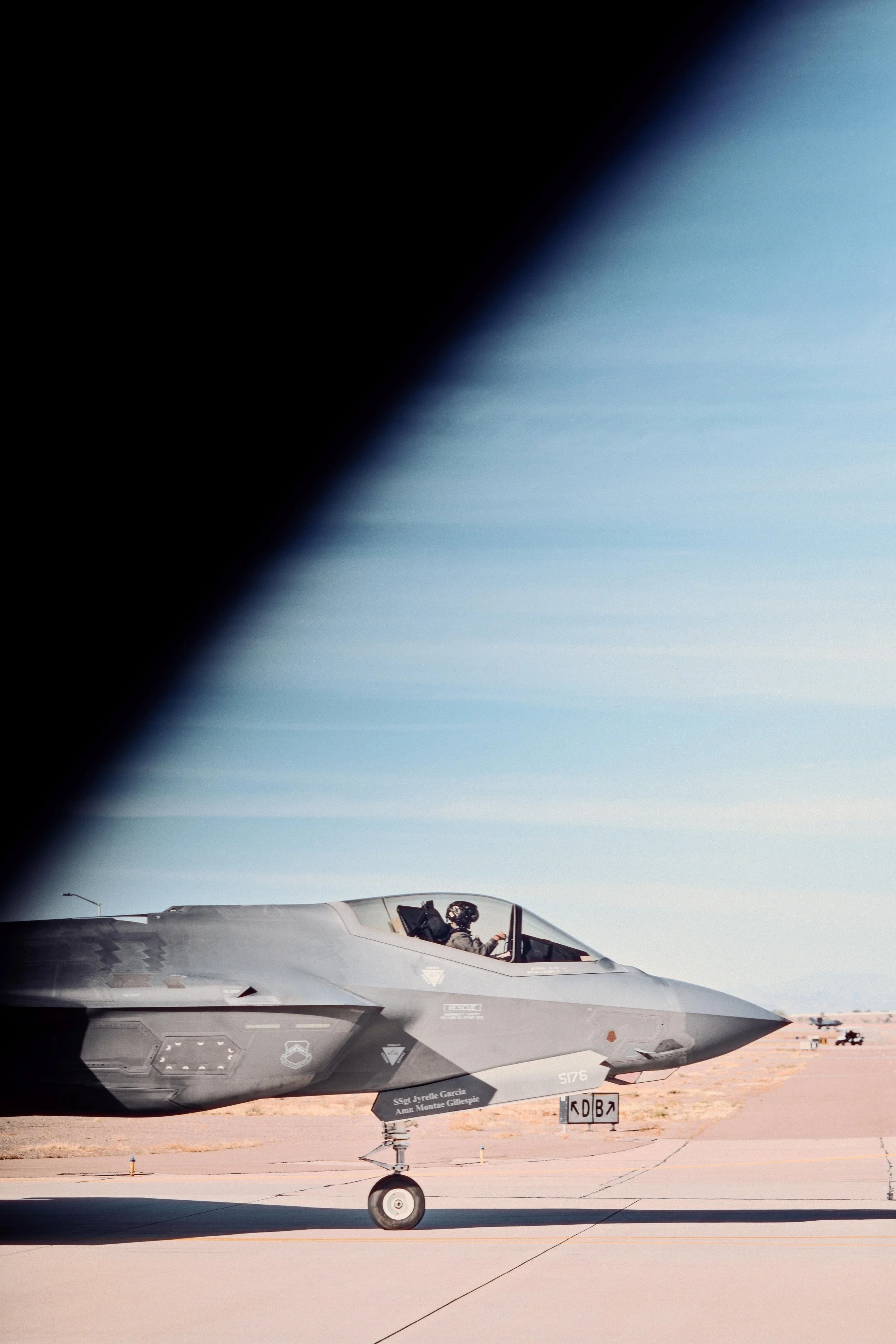 An F-35 fighter jet on the tarmac at an airbase, with a person in the cockpit and a clear sky in the background.