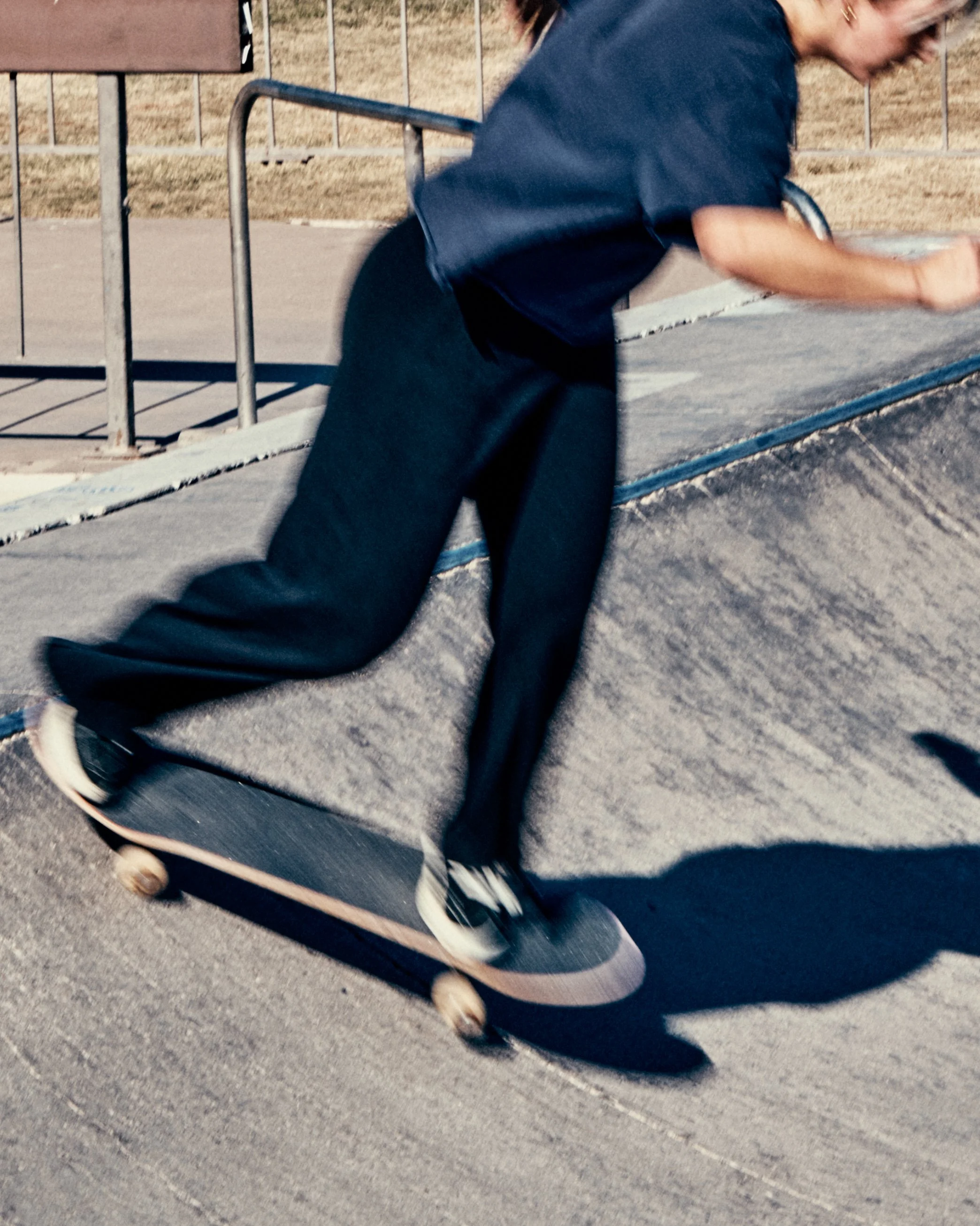 Person skateboarding at a skatepark, wearing dark clothing and black sneakers.
