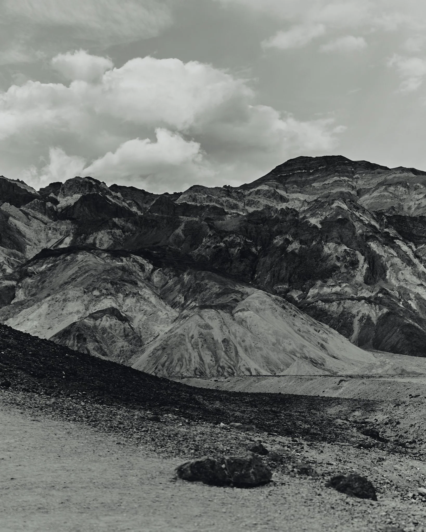 Black and white photo of rugged mountain landscape with multiple layers of rocky hills and mountains under cloudy sky.