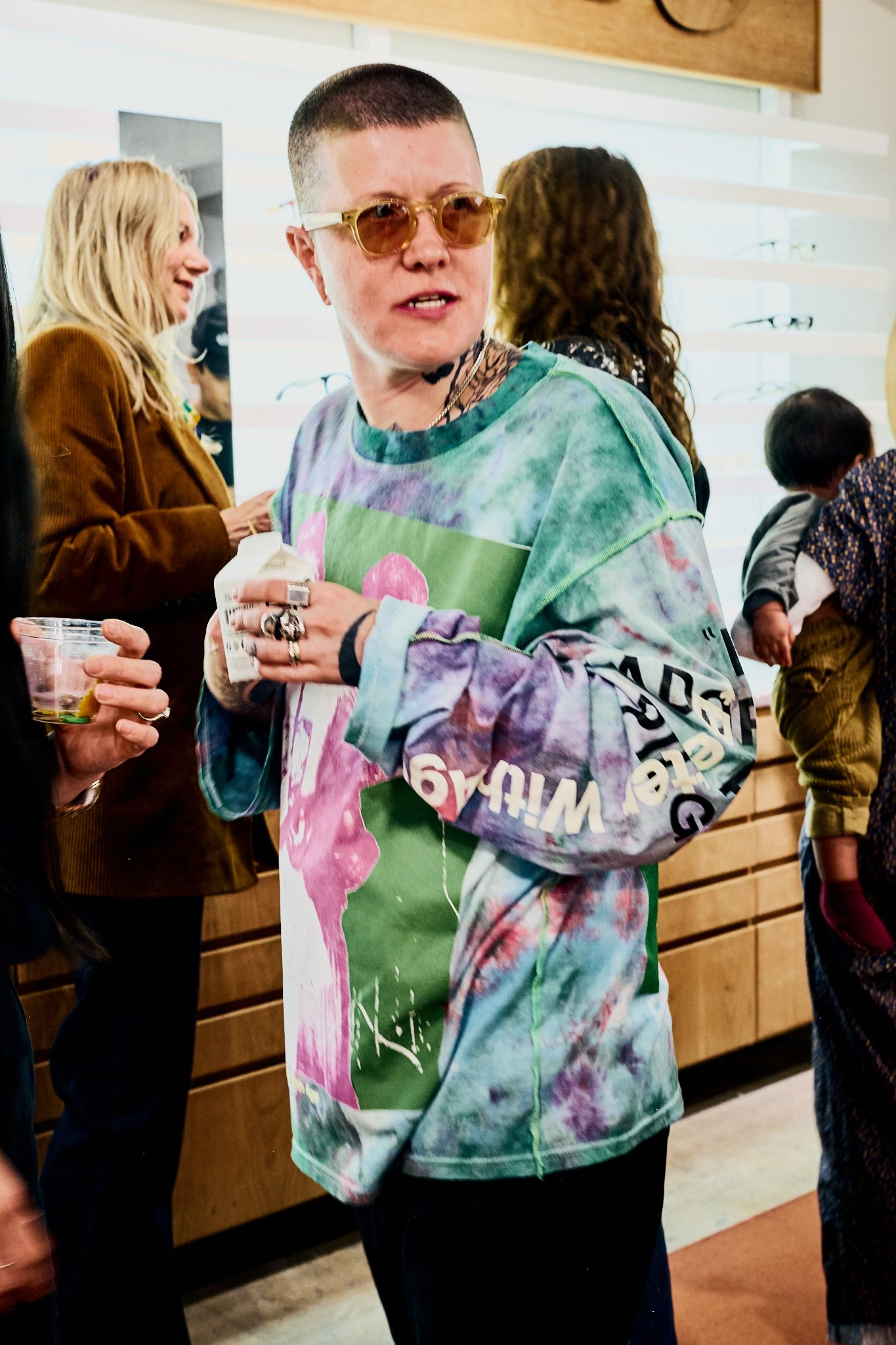 Person wearing sunglasses and a colorful tie-dye sweatshirt at social gathering.