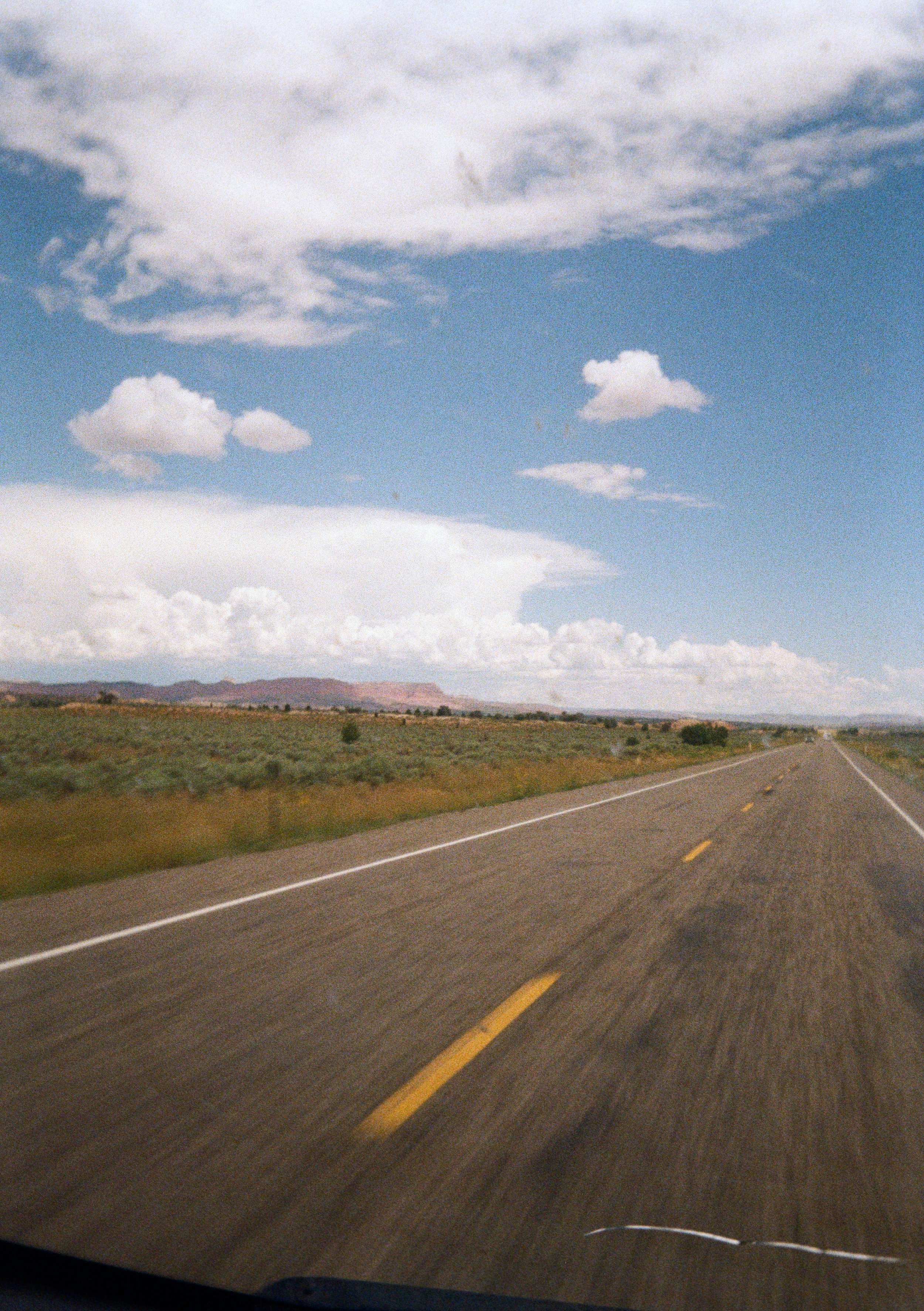 Open road extending to the horizon through a flat, open landscape with a blue sky and scattered clouds.