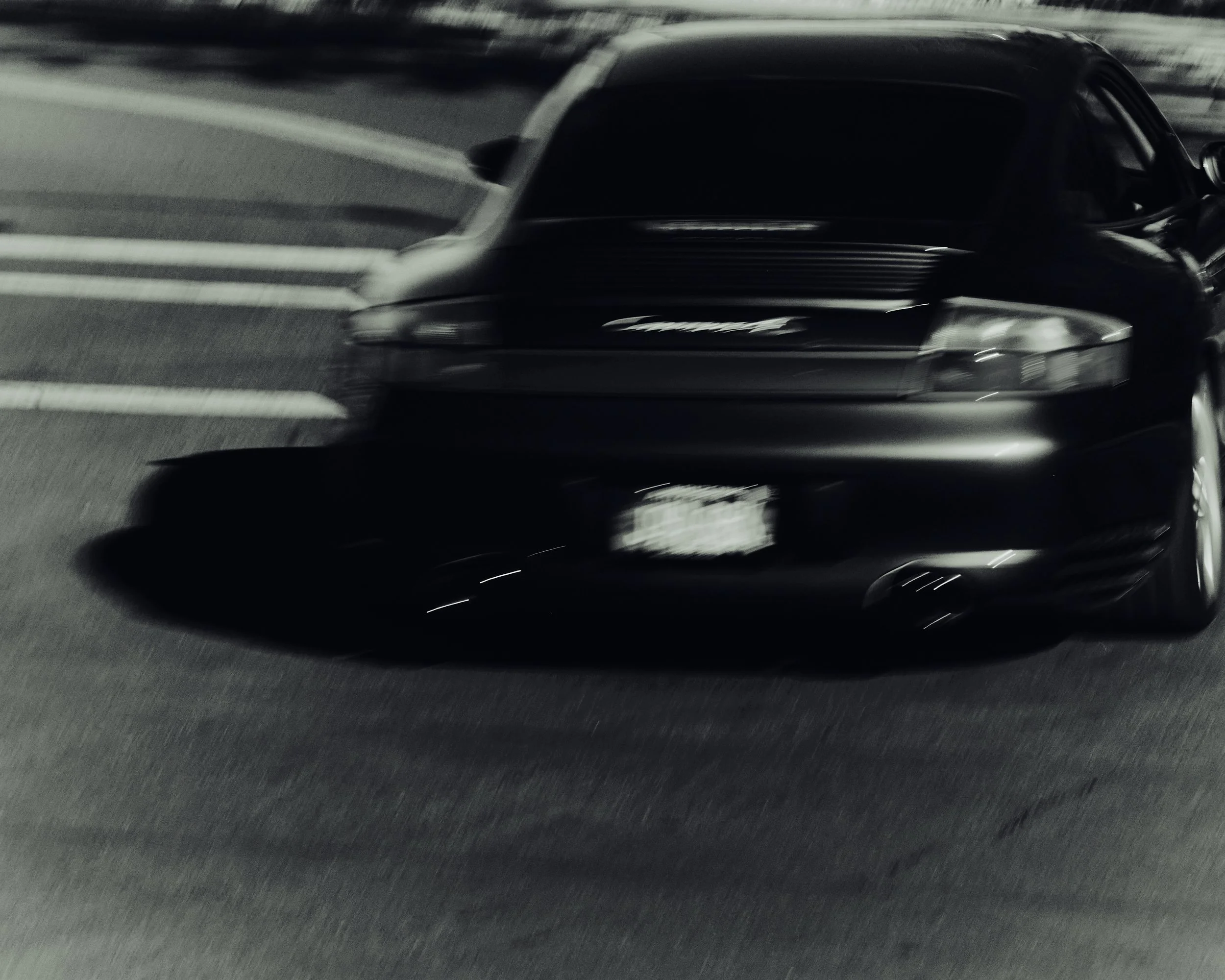 A black sports car driving at night on a road with streetlights, captured with motion blur.