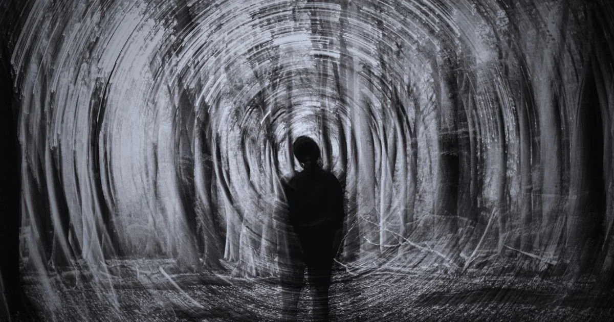 Abstract black and white silhouette of a person standing in a forest with a swirling, motion-blur tunnel effect, representing the internal experience of a panic disorder and sensory overload.