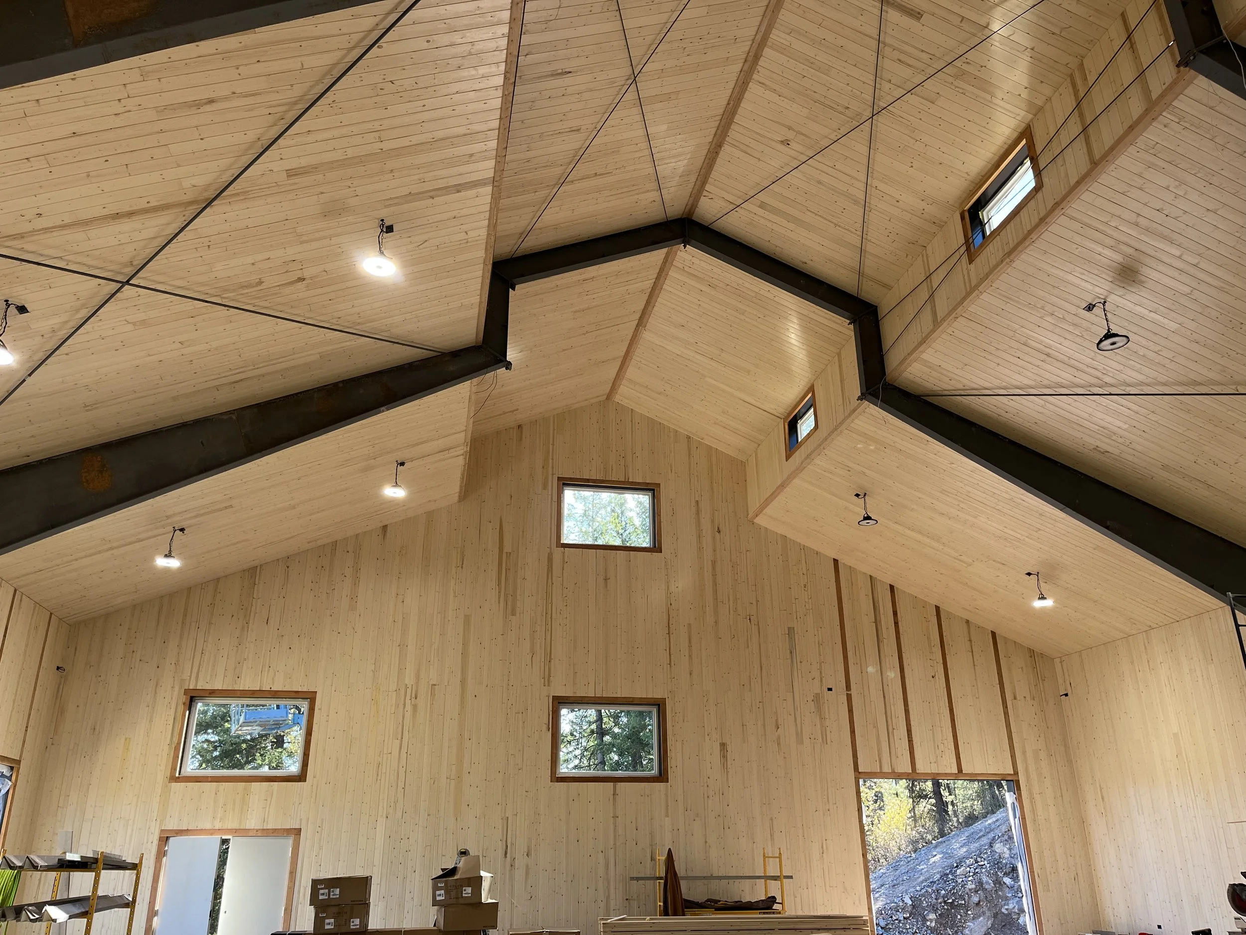 Interior of a wooden building with high vaulted ceiling, several small windows, and construction materials inside.