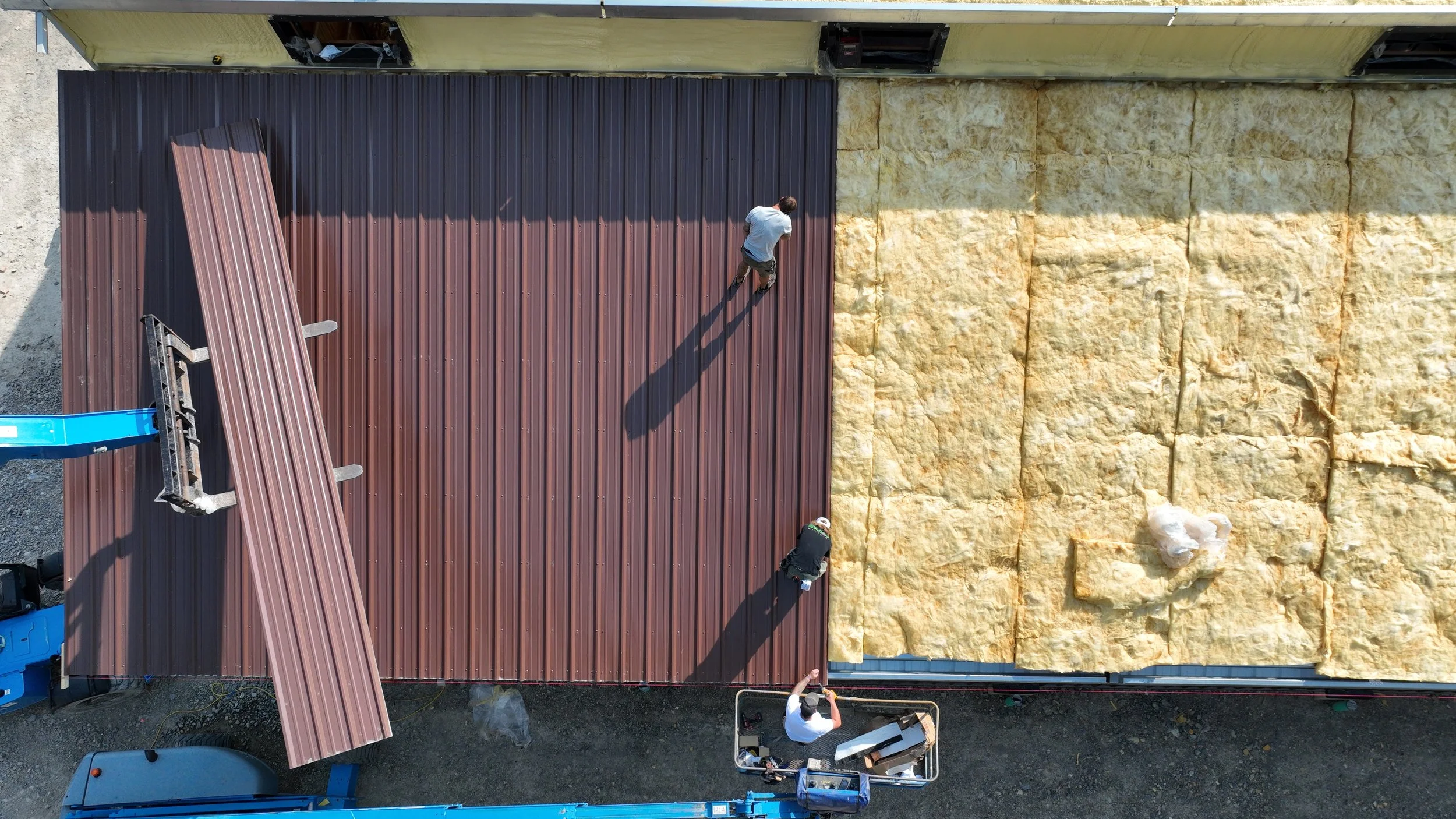 Two workers installing metal roofing panels while other materials and tools are nearby.