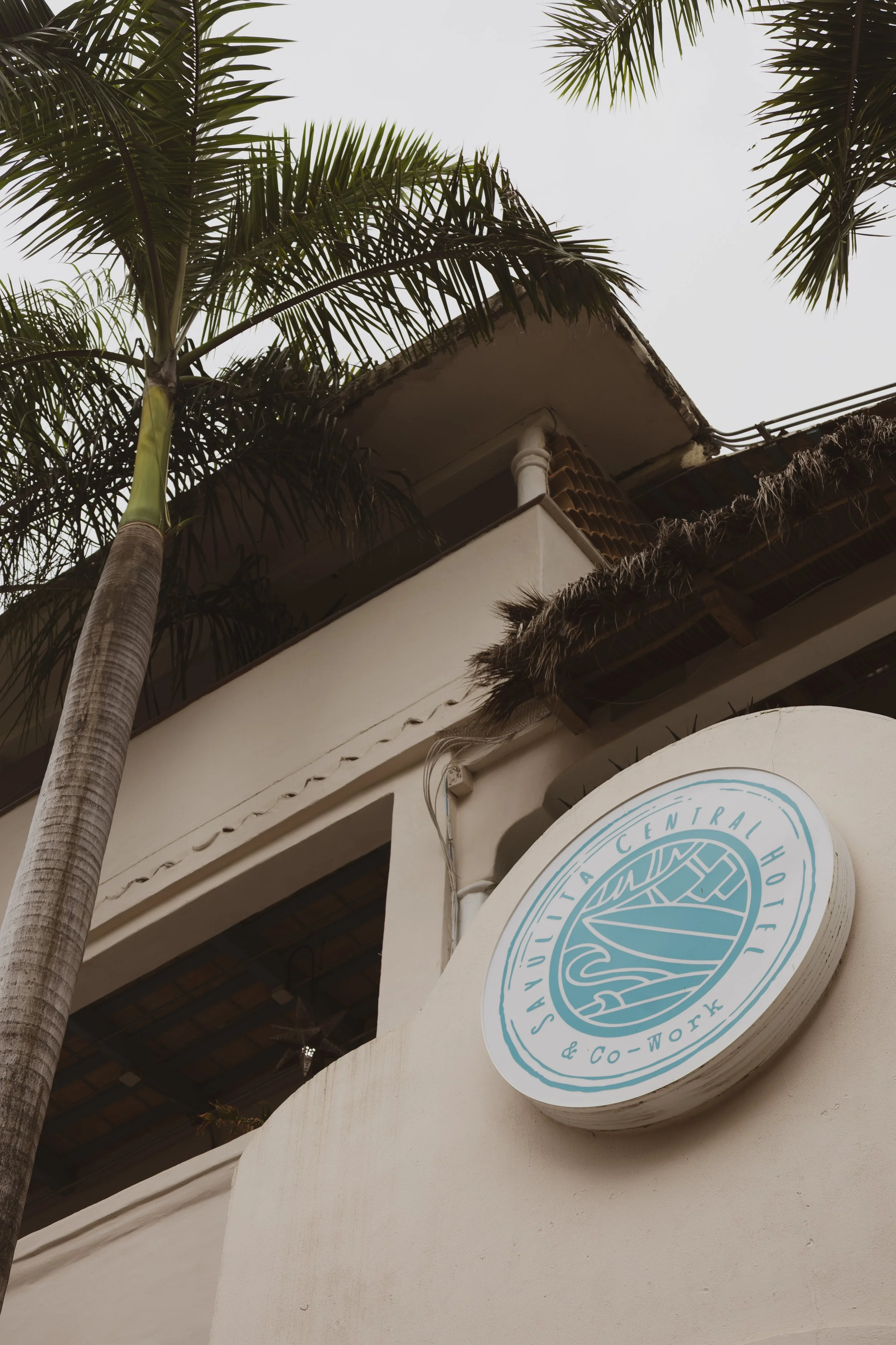 Exterior of a building with a circular sign reading 'Central Hotel & Co-Work' and palm trees nearby.