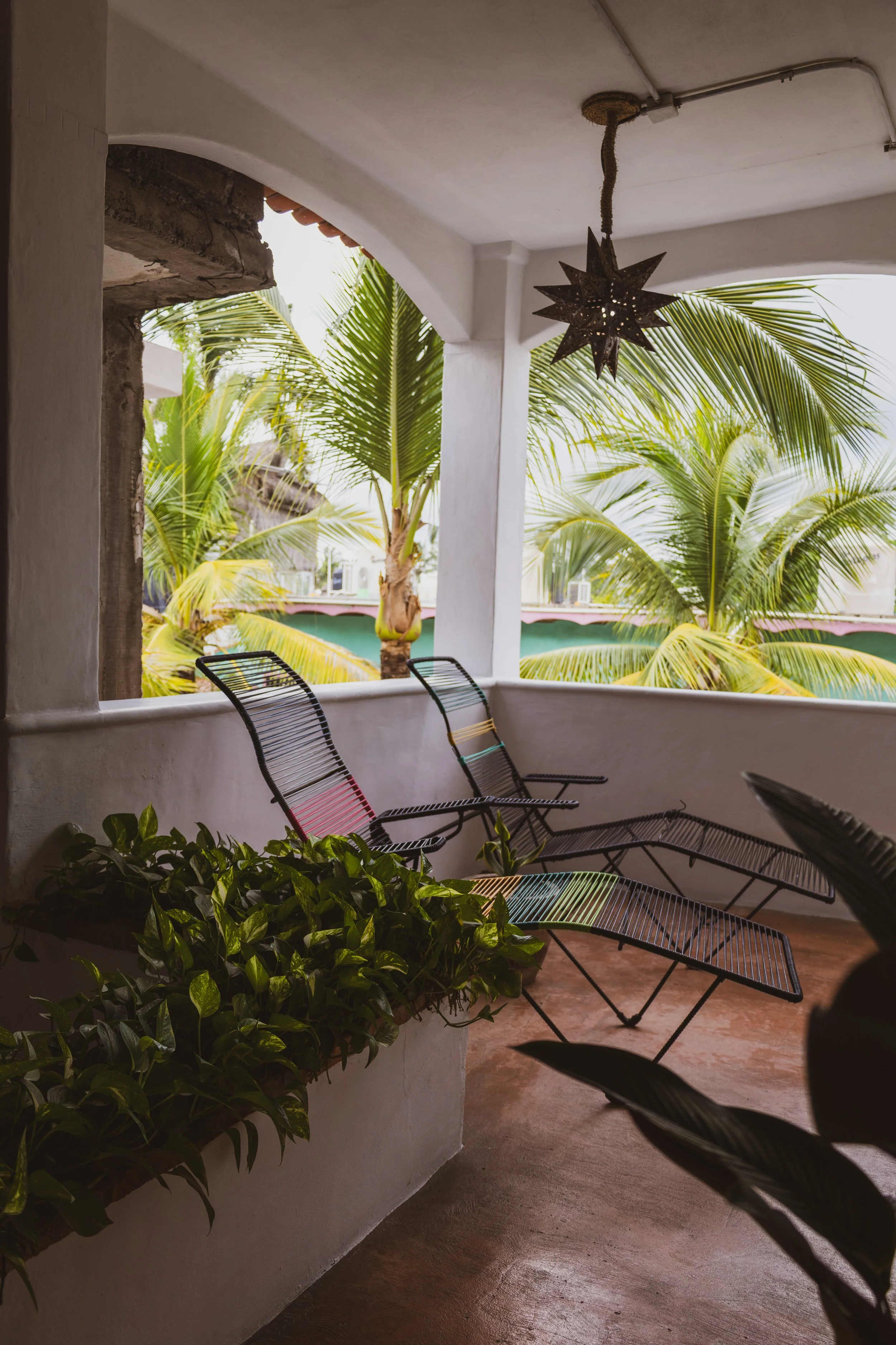 Balcony with green palm trees, black metal chairs, and a star-shaped hanging lamp.