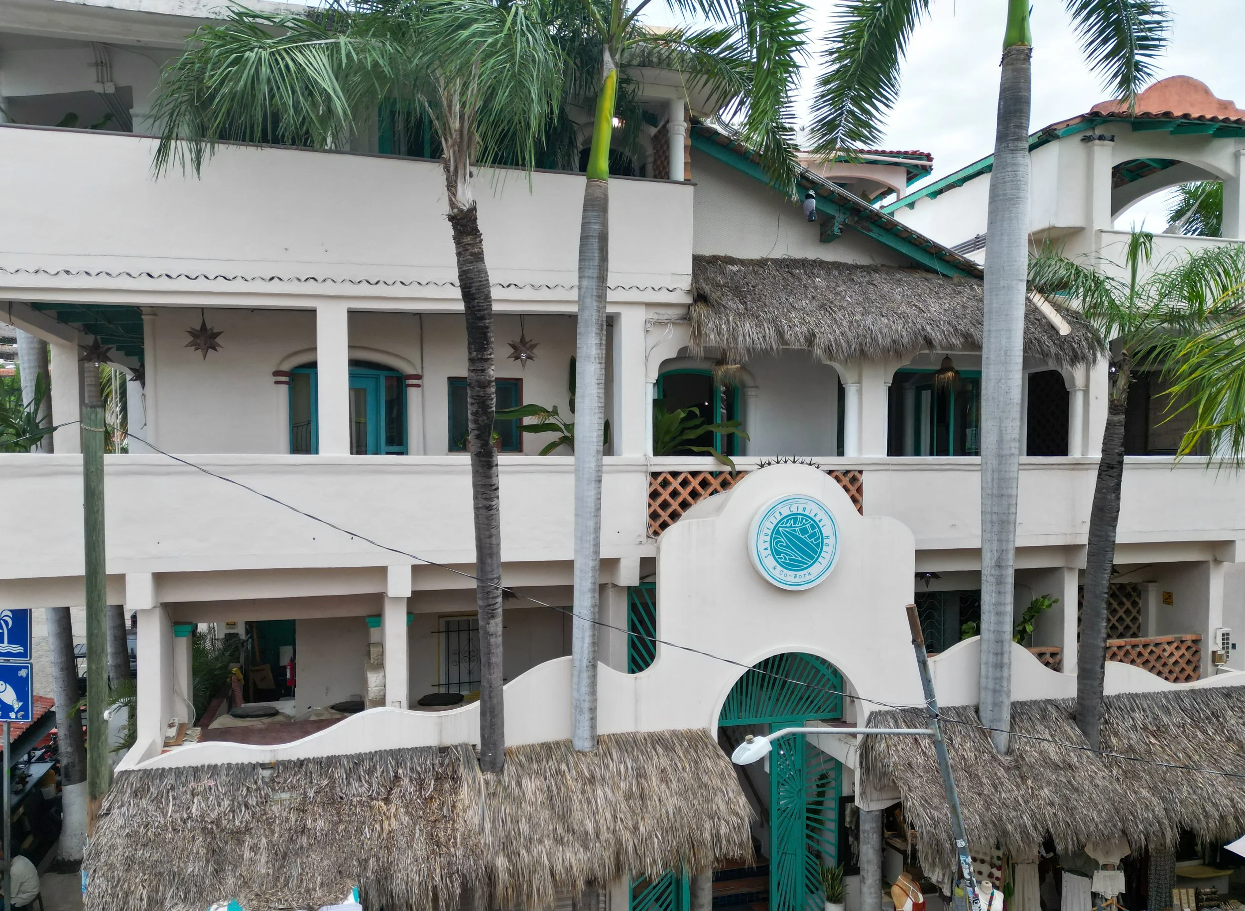 Multiple buildings with tropical architecture and thatched roofs, surrounded by palm trees.