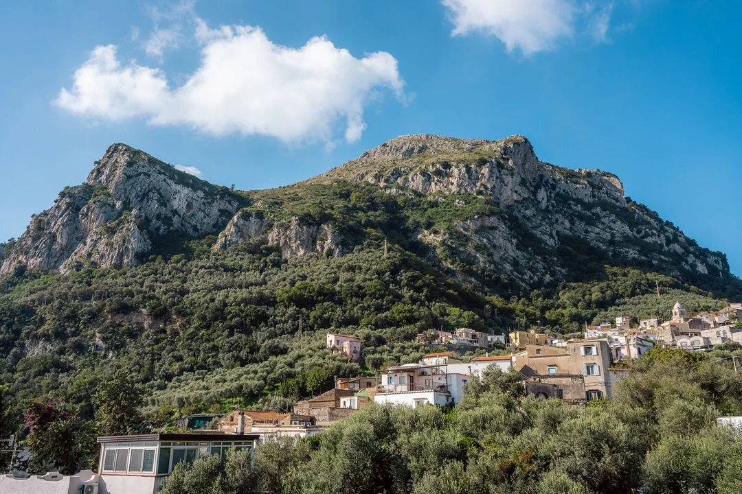 Scenic mountain with a small town and green trees at its base under a partly cloudy blue sky.