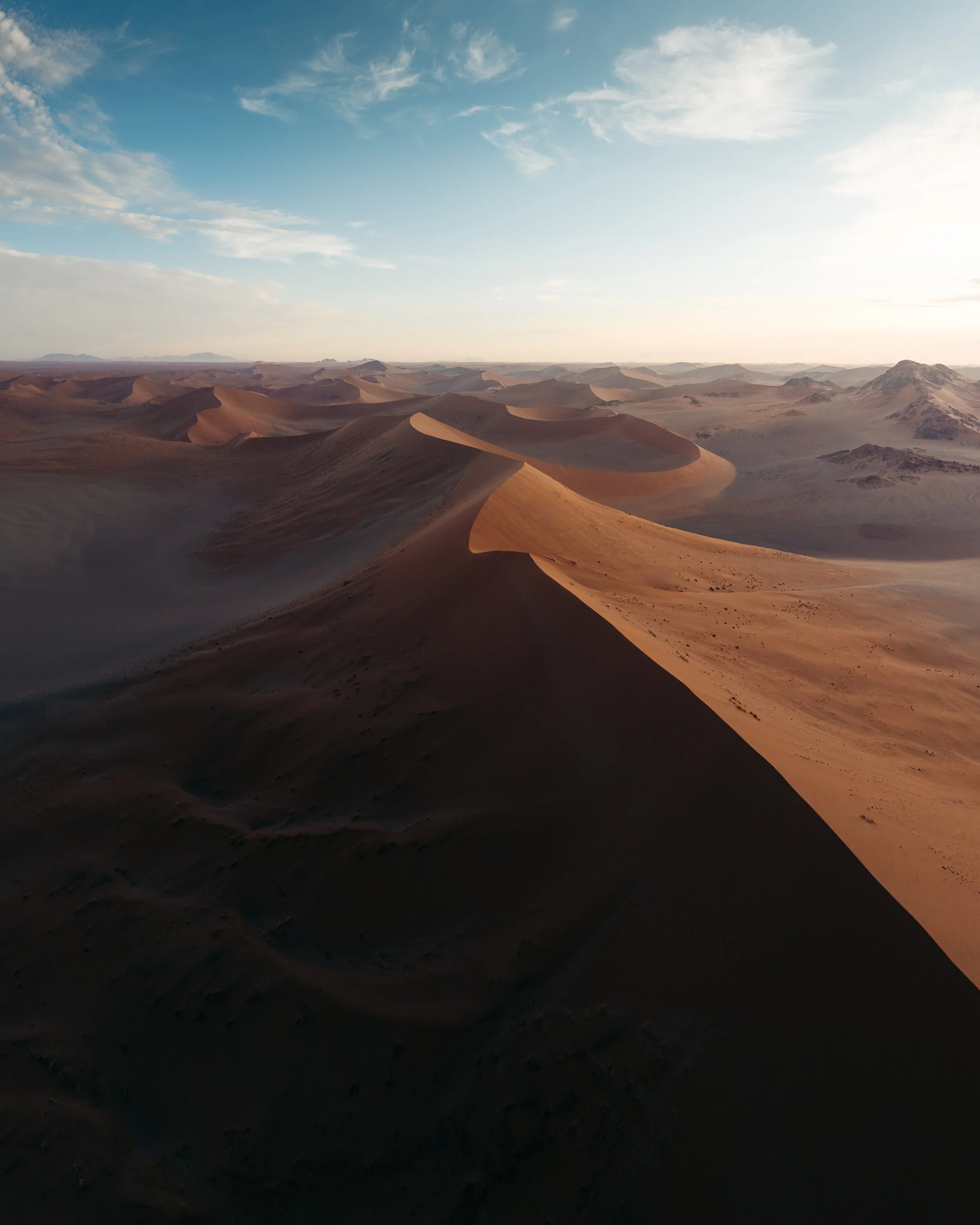 A vast desert with large sand dunes under a partly cloudy sky.