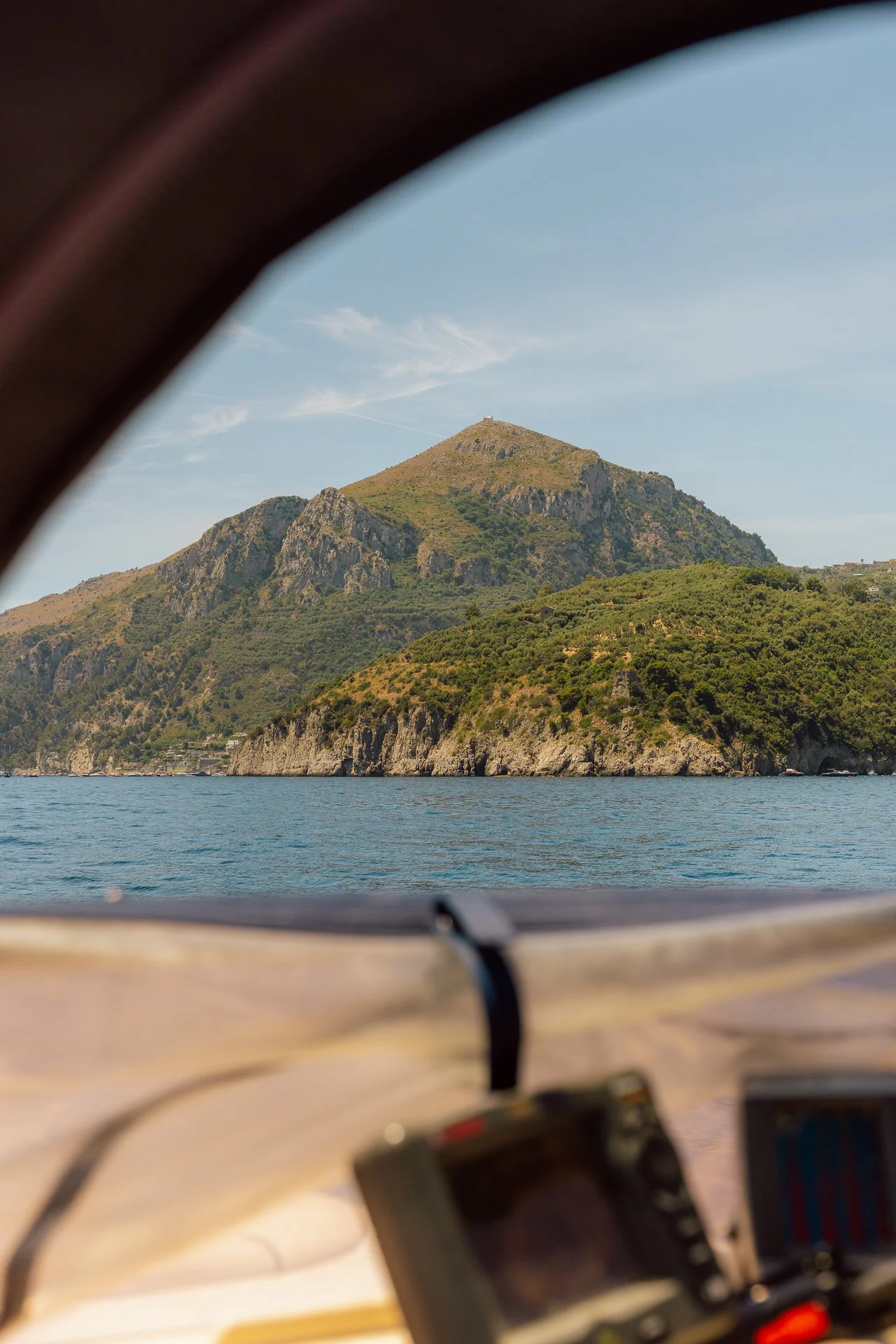 View of a mountainous island seen from a boat, framed by the boat's window and dashboard in the foreground.
