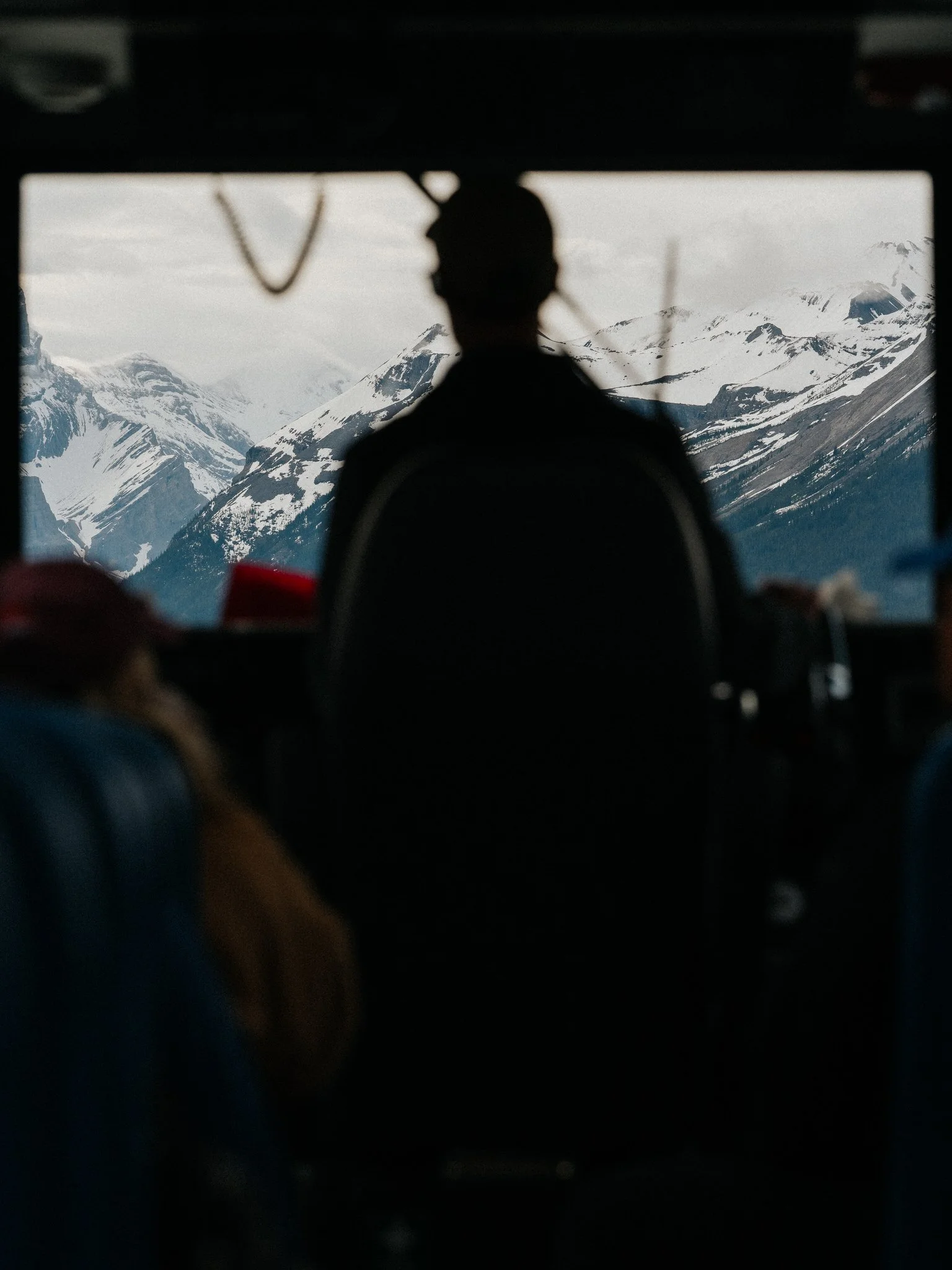 Silhouette of a person looking out the window at snow-covered mountains.