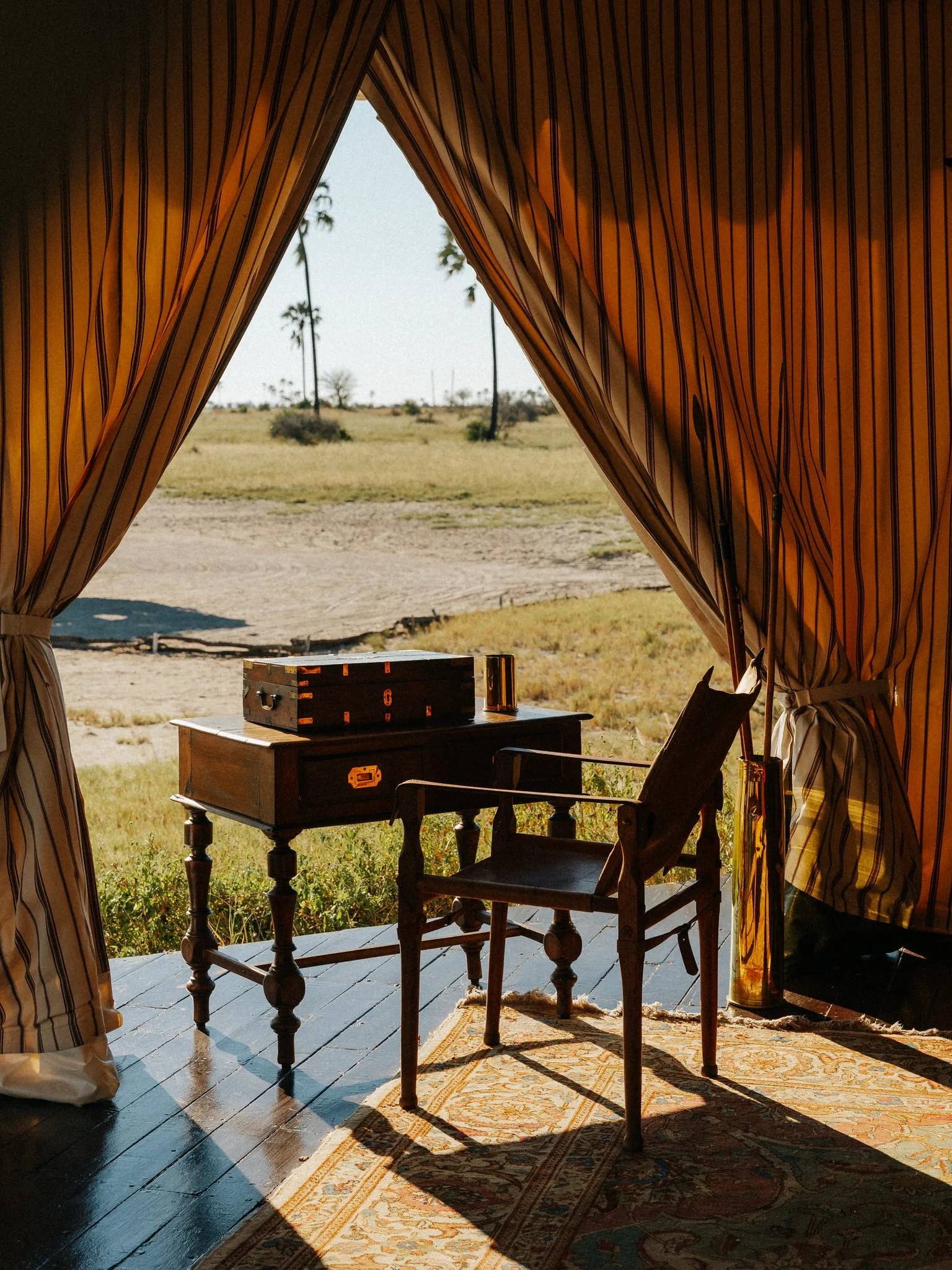 View through an open door with striped curtains showing a grassy outdoor area with palm trees and a clear sky.