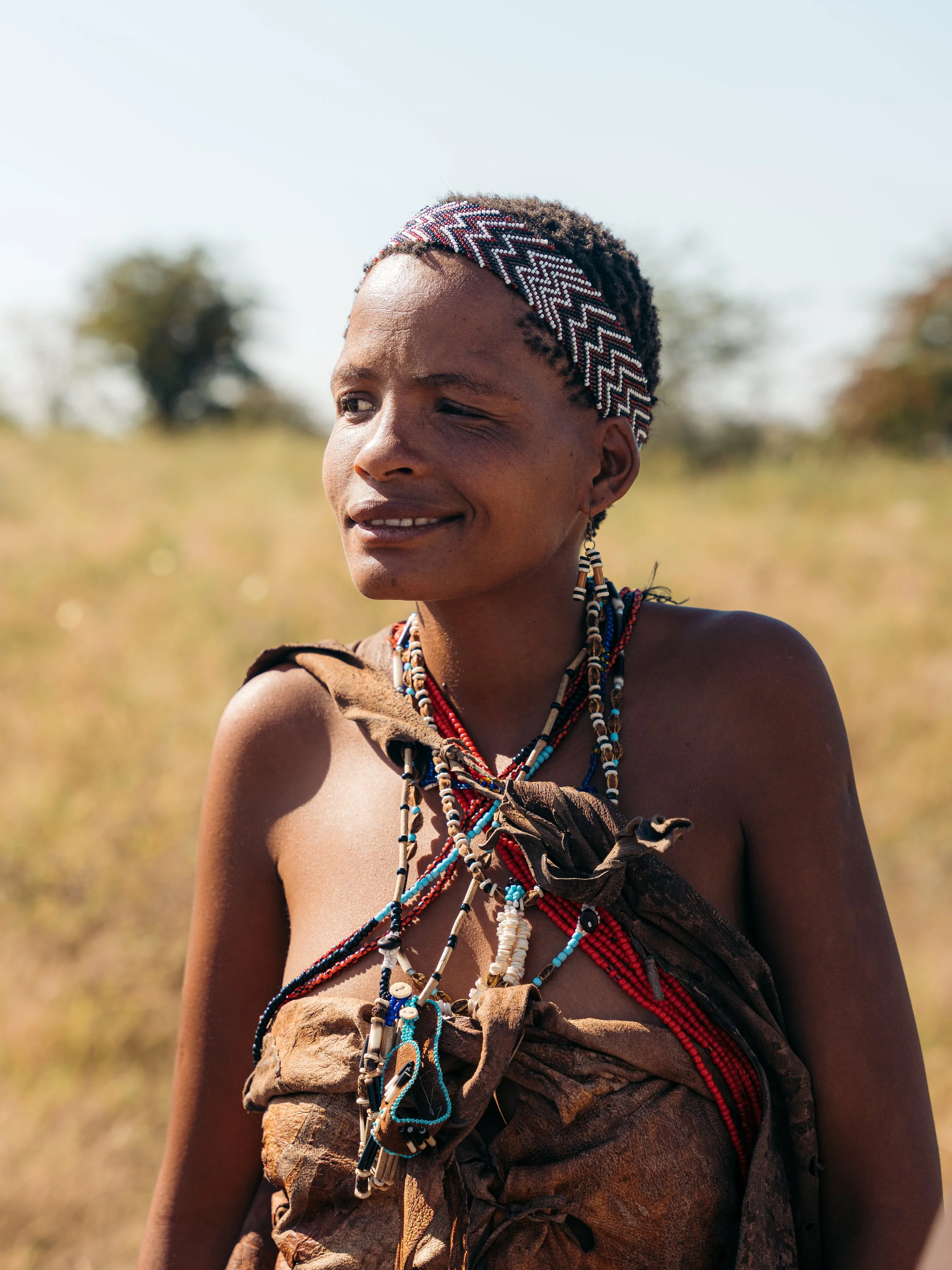 Portrait of an indigenous woman wearing traditional beaded jewelry and a patterned headband, standing outdoors in a natural landscape.