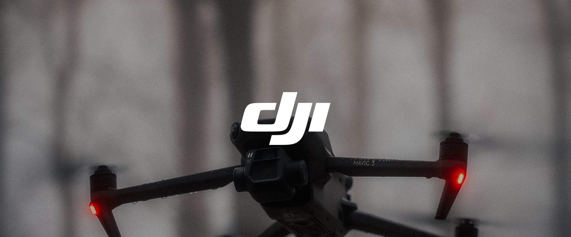 Close-up of a DJI drone with the DJI logo on top, flying outdoors with a blurred background, showing red lights on the arms.