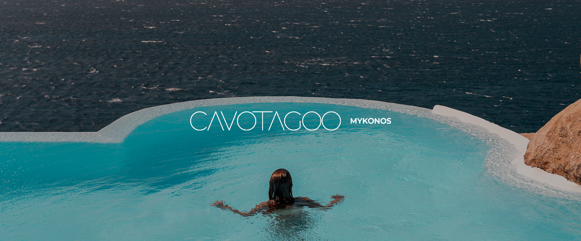 A person swimming in a blue pool with the ocean in the background, featuring the text "CAVOTAGO MYKONOS" on the pool's edge.