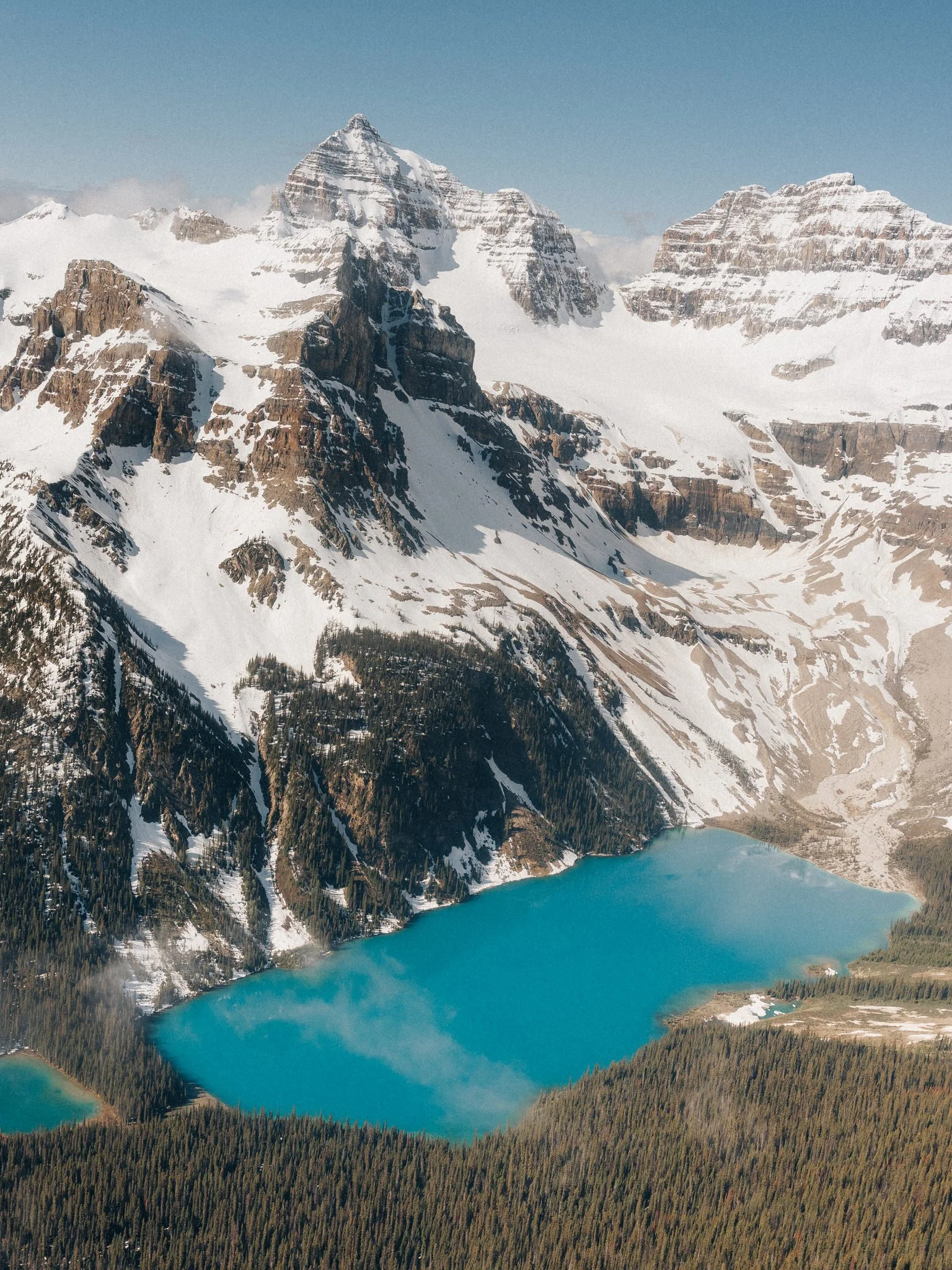 Snow-capped mountains with a turquoise lake at the base, surrounded by forests.