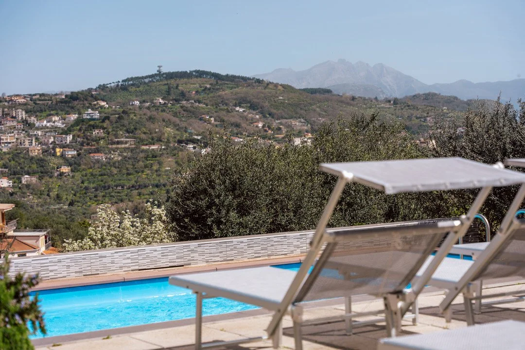 Poolside view with lounge chairs overlooking a mountainous landscape with trees, houses, and distant mountains.