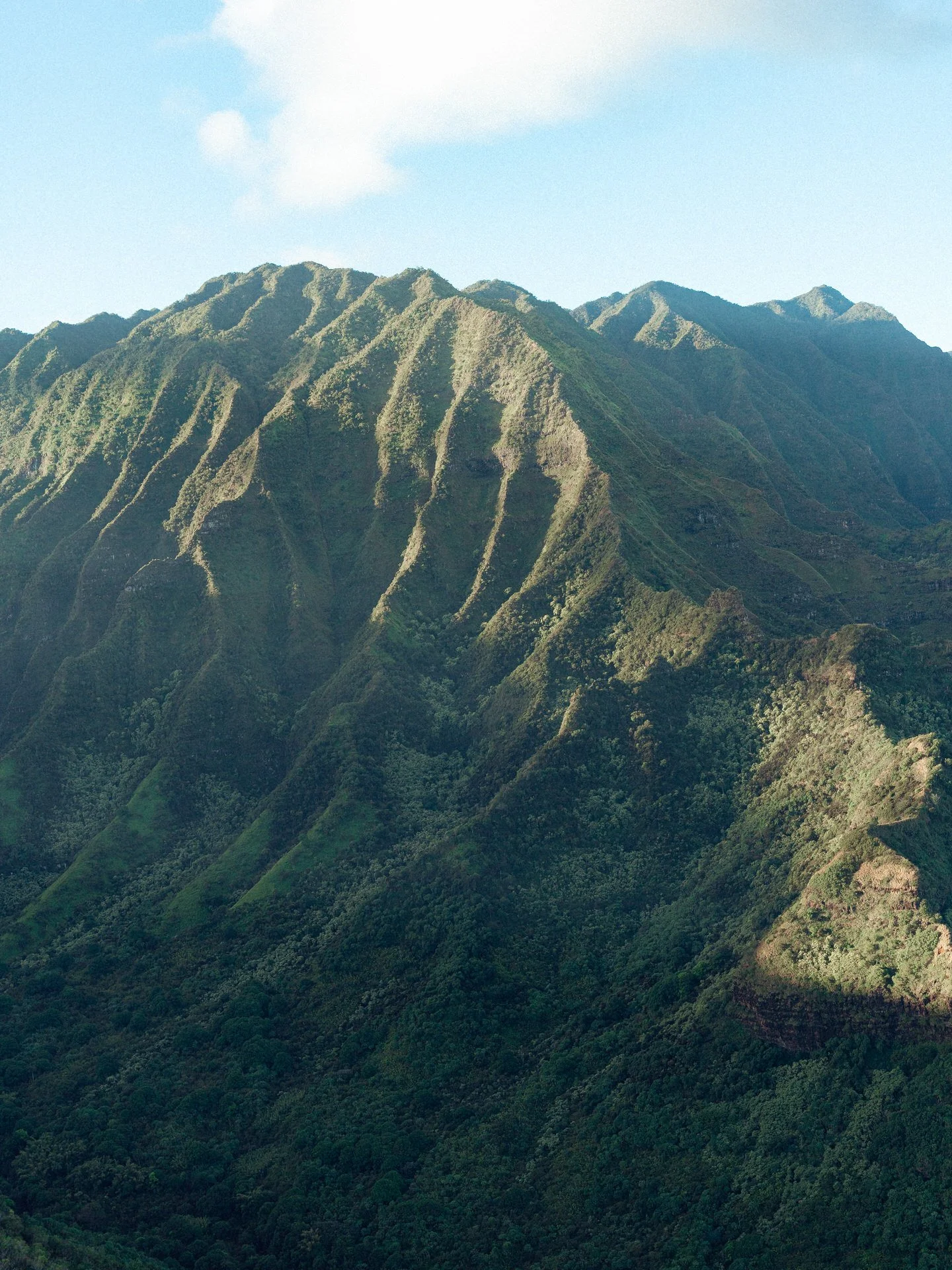 Green mountainous landscape with steep ridges under a partly cloudy sky.