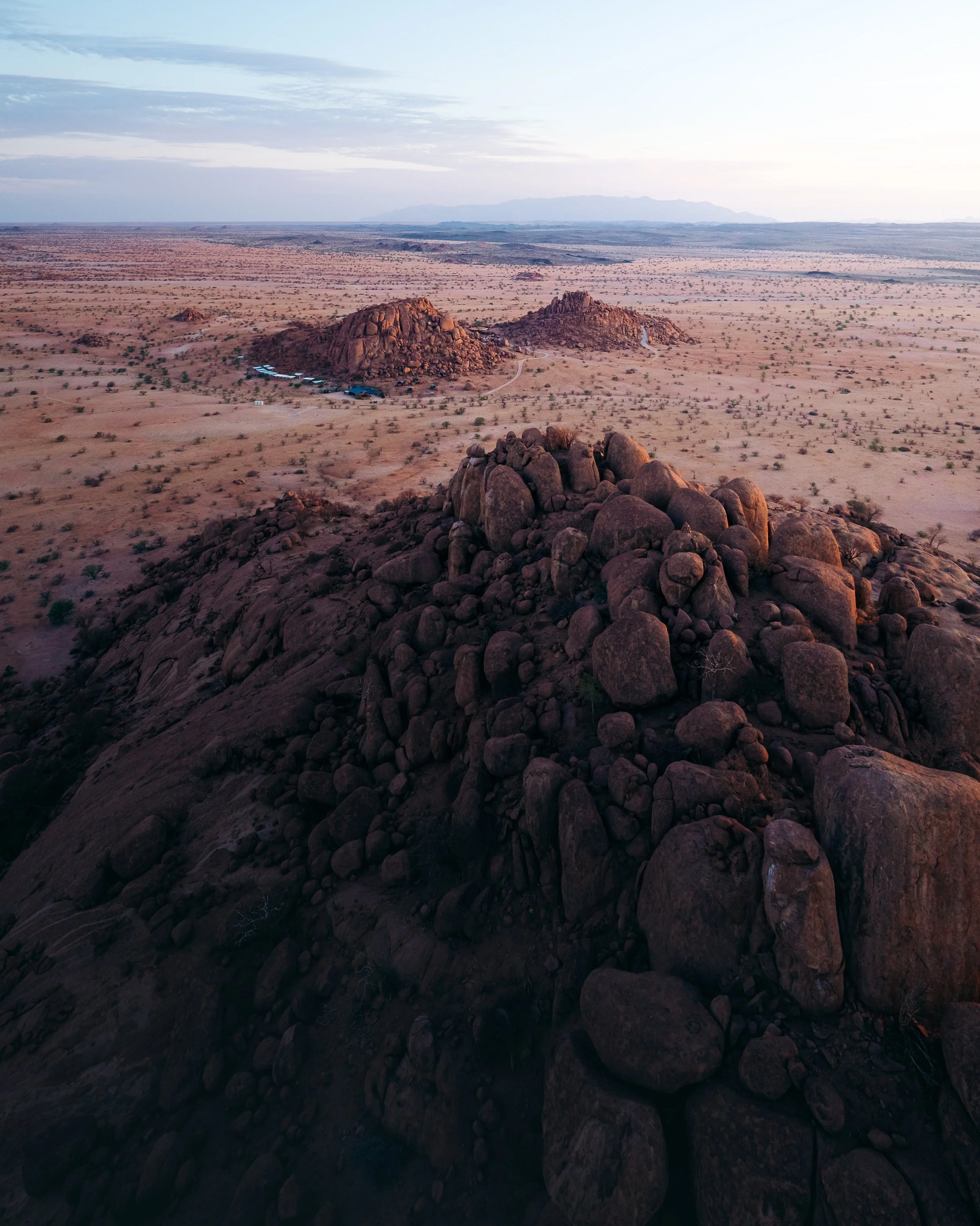 Aerial view of rocky desert landscape with large boulders and sparse vegetation, possibly in a southwestern region of the United States, during sunset or twilight.