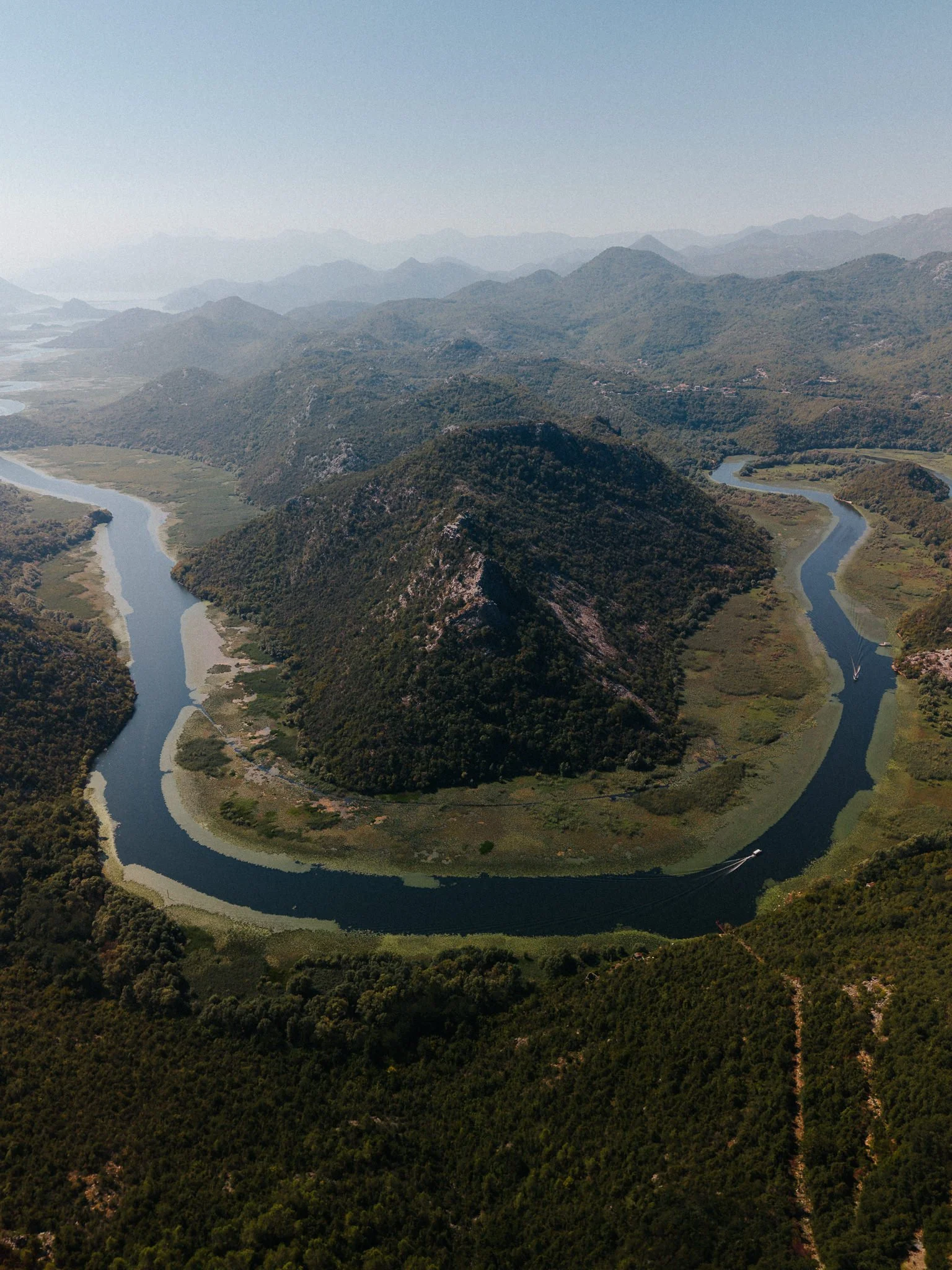 Aerial view of a winding river flowing through a green mountainous landscape under a clear sky.