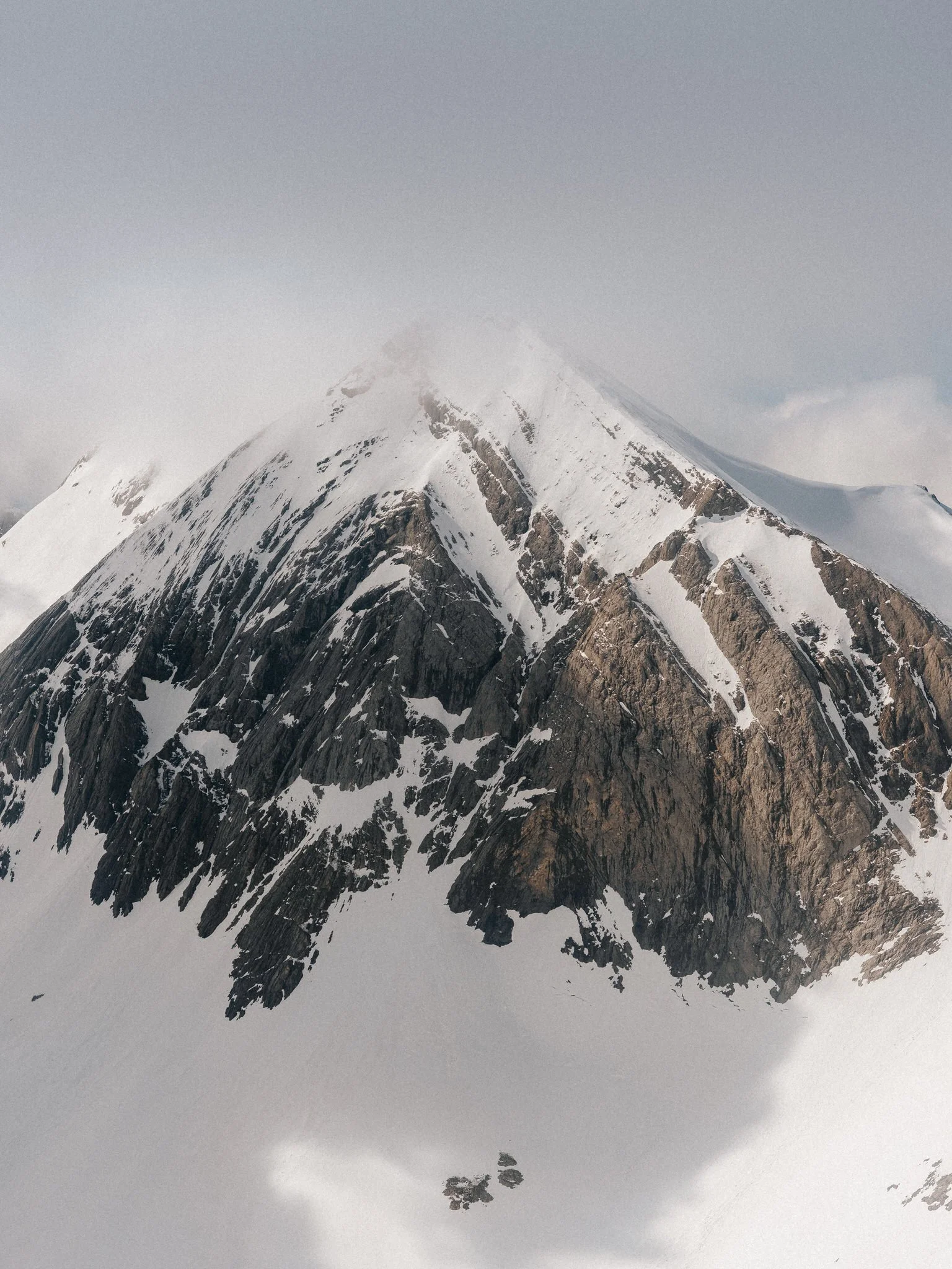 Snow-covered mountain peak with rocky slopes and a cloudy sky.