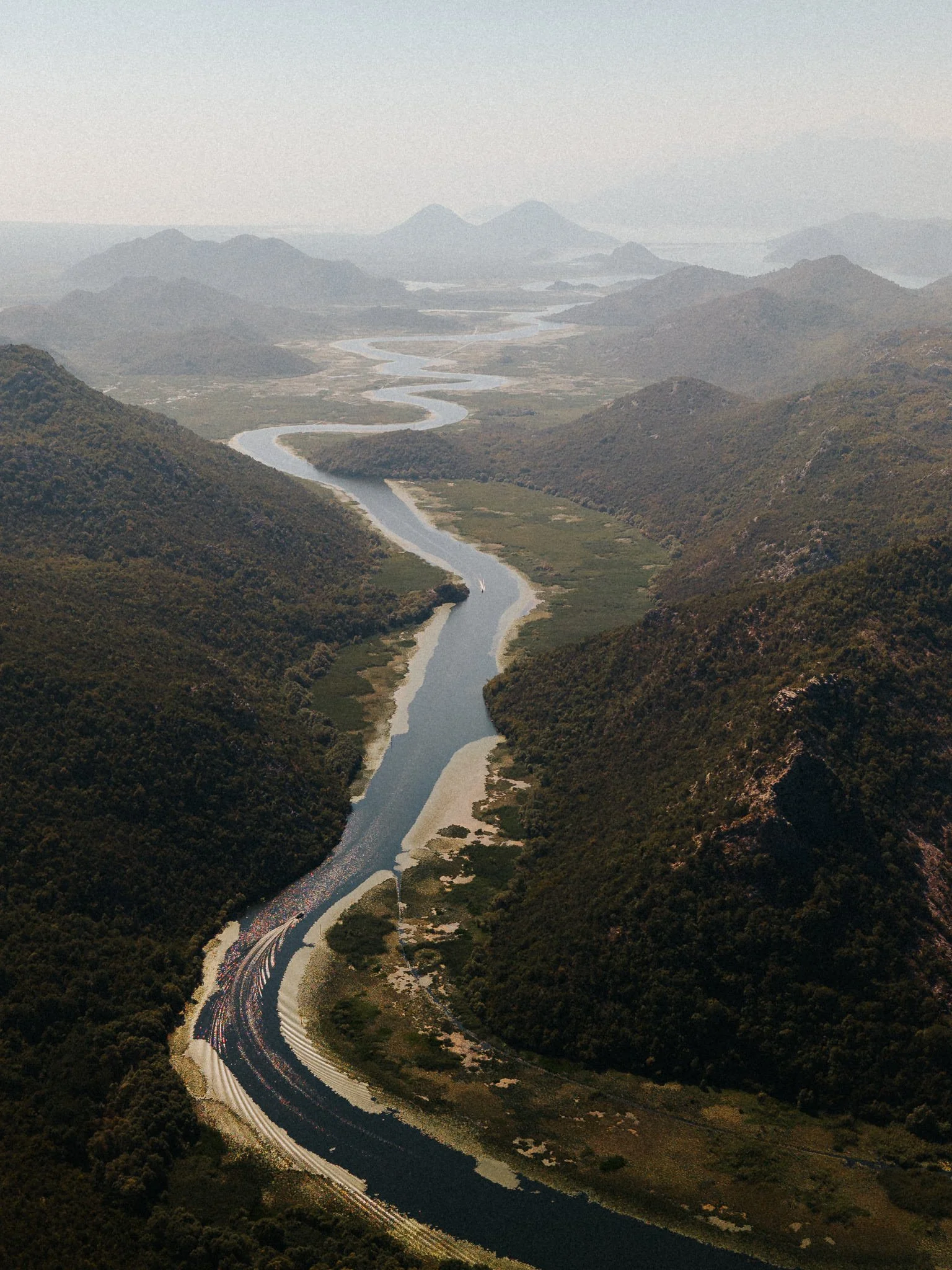 A winding river flowing through a valley surrounded by green mountains under a gray sky.