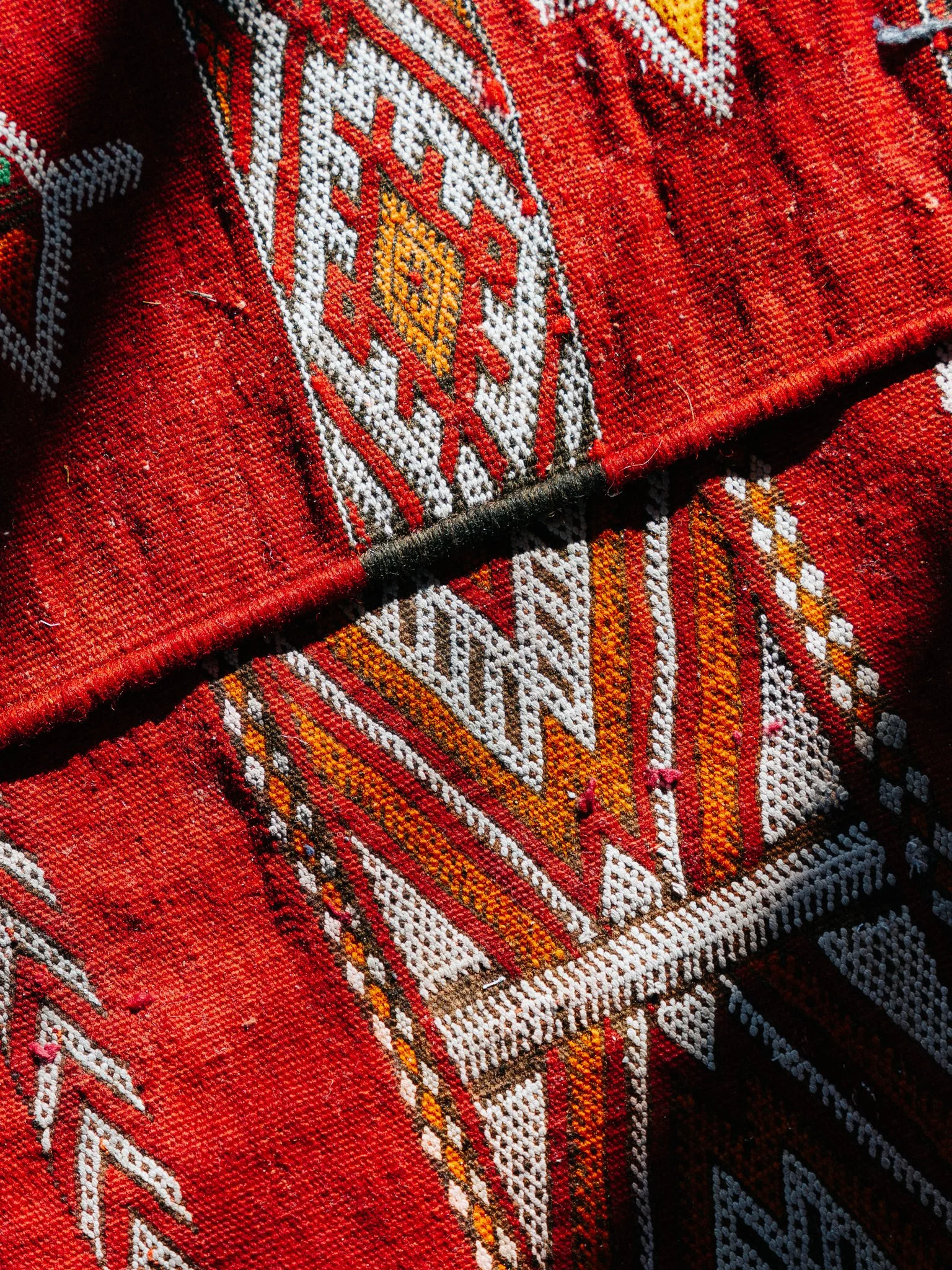 Close-up of a detailed, colorful woven textile with geometric patterns in red, white, yellow, black, and orange.