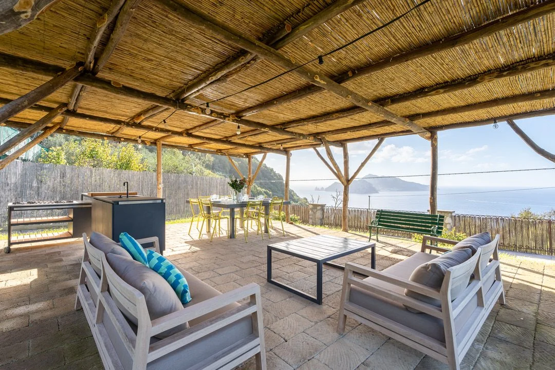 Outdoor patio with seating, a dining table, and a view of the ocean and distant hills.