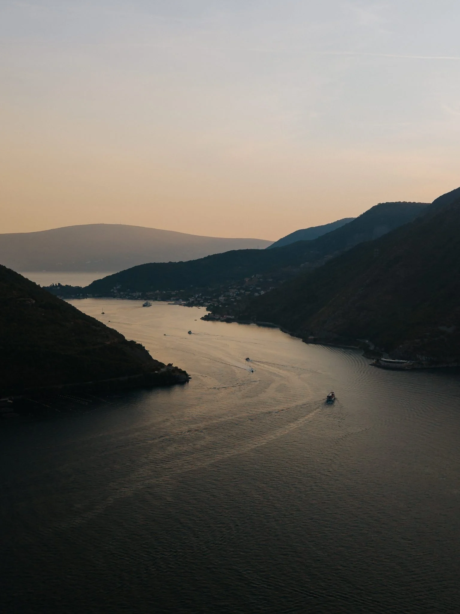 A river flowing through hills and mountains at sunset, with several boats visible on the water.