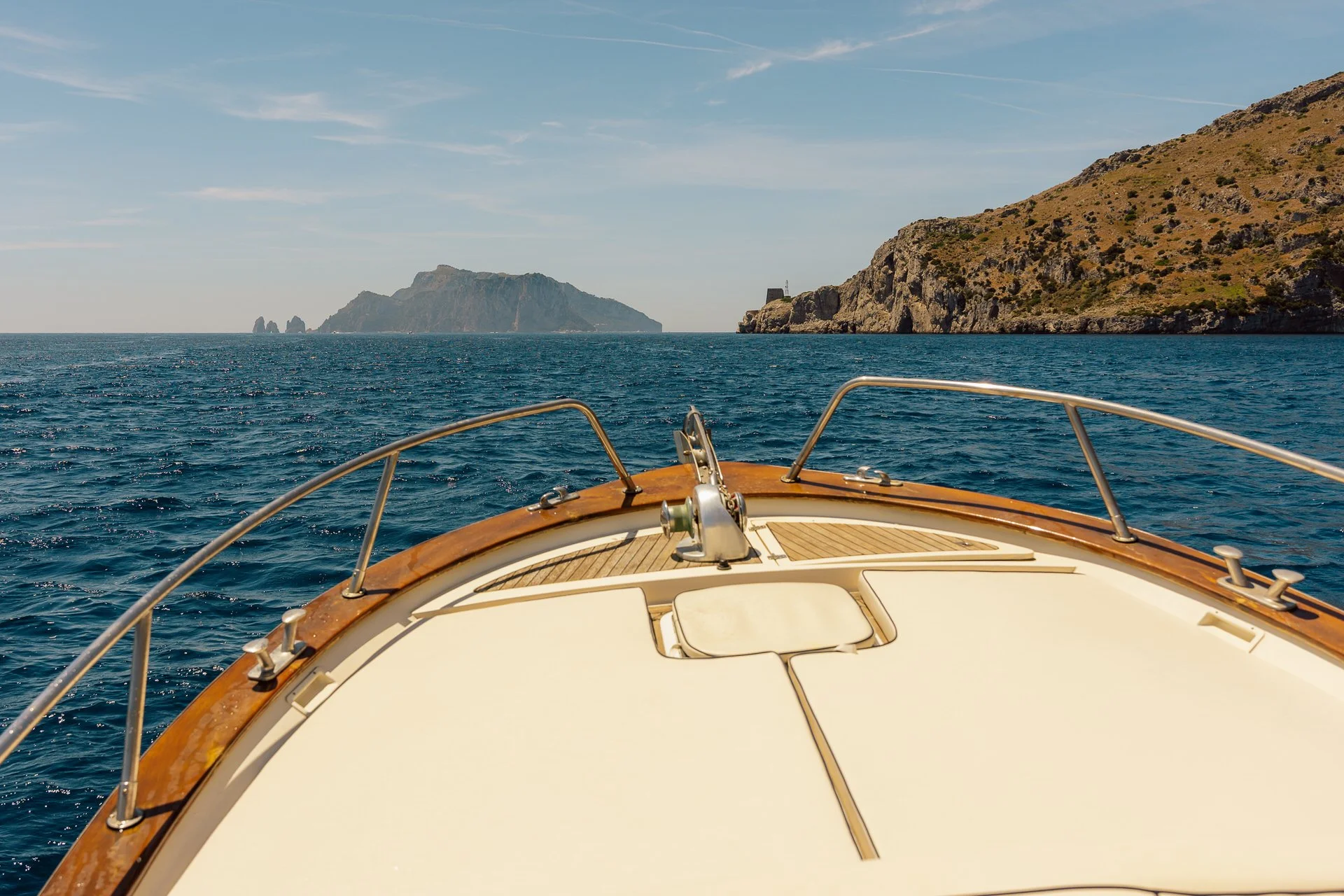 Front of a boat on open water with land and cliffs in the distance.