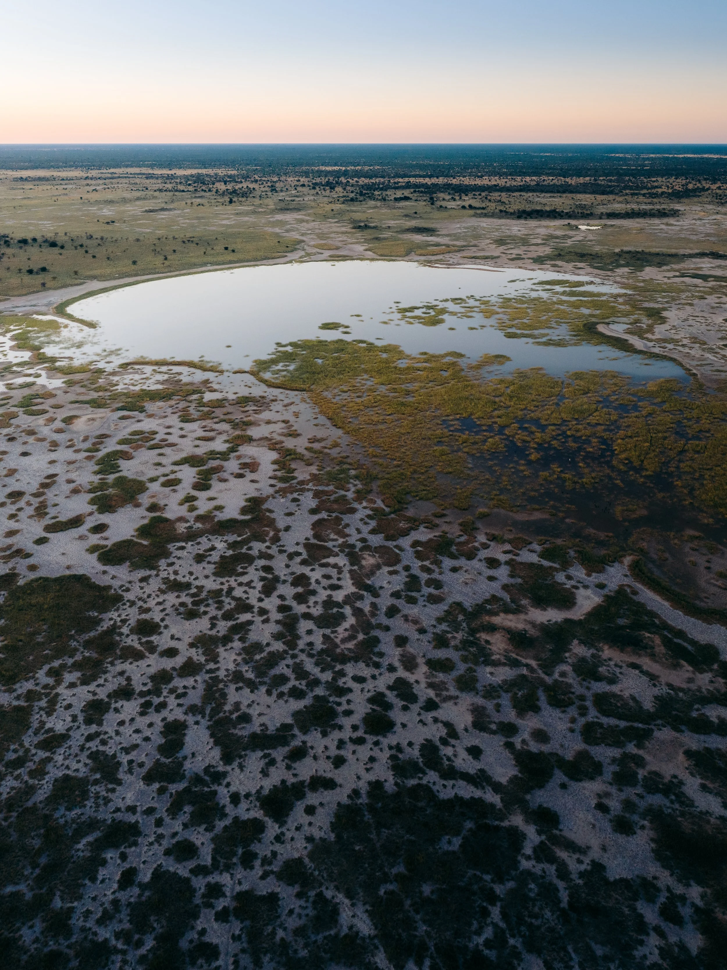 Aerial view of a wetland with a large pond surrounded by marshy areas and sparse vegetation, under a twilight sky.