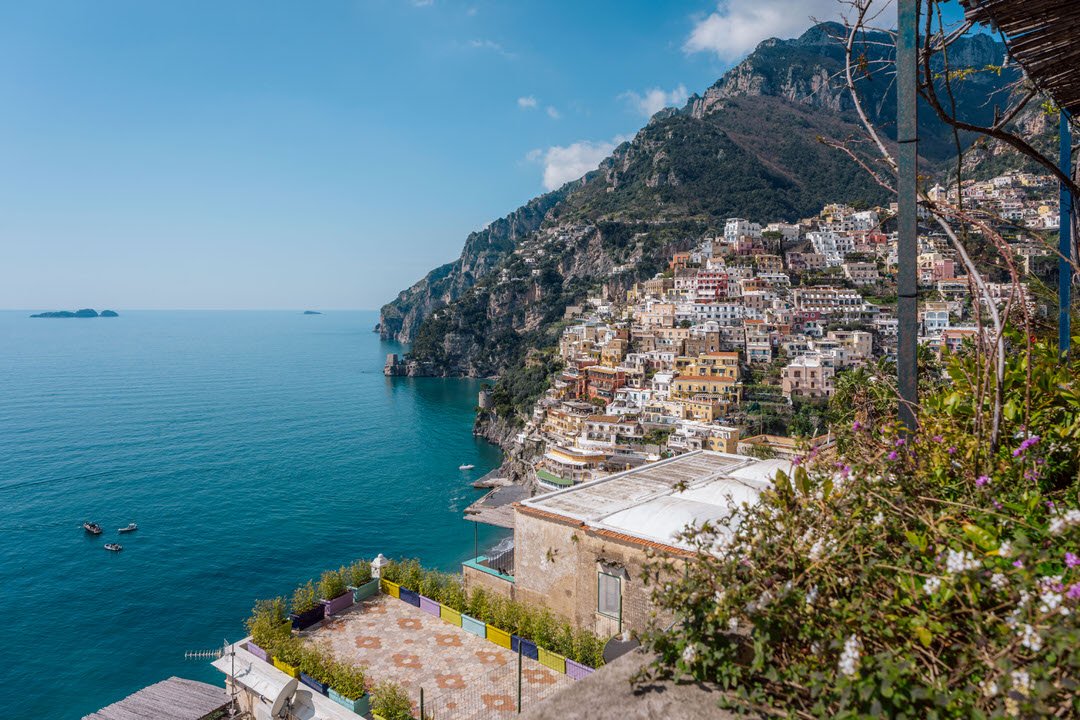 Colorful buildings along a steep hillside overlooking the ocean with small boats and islands in the distance.