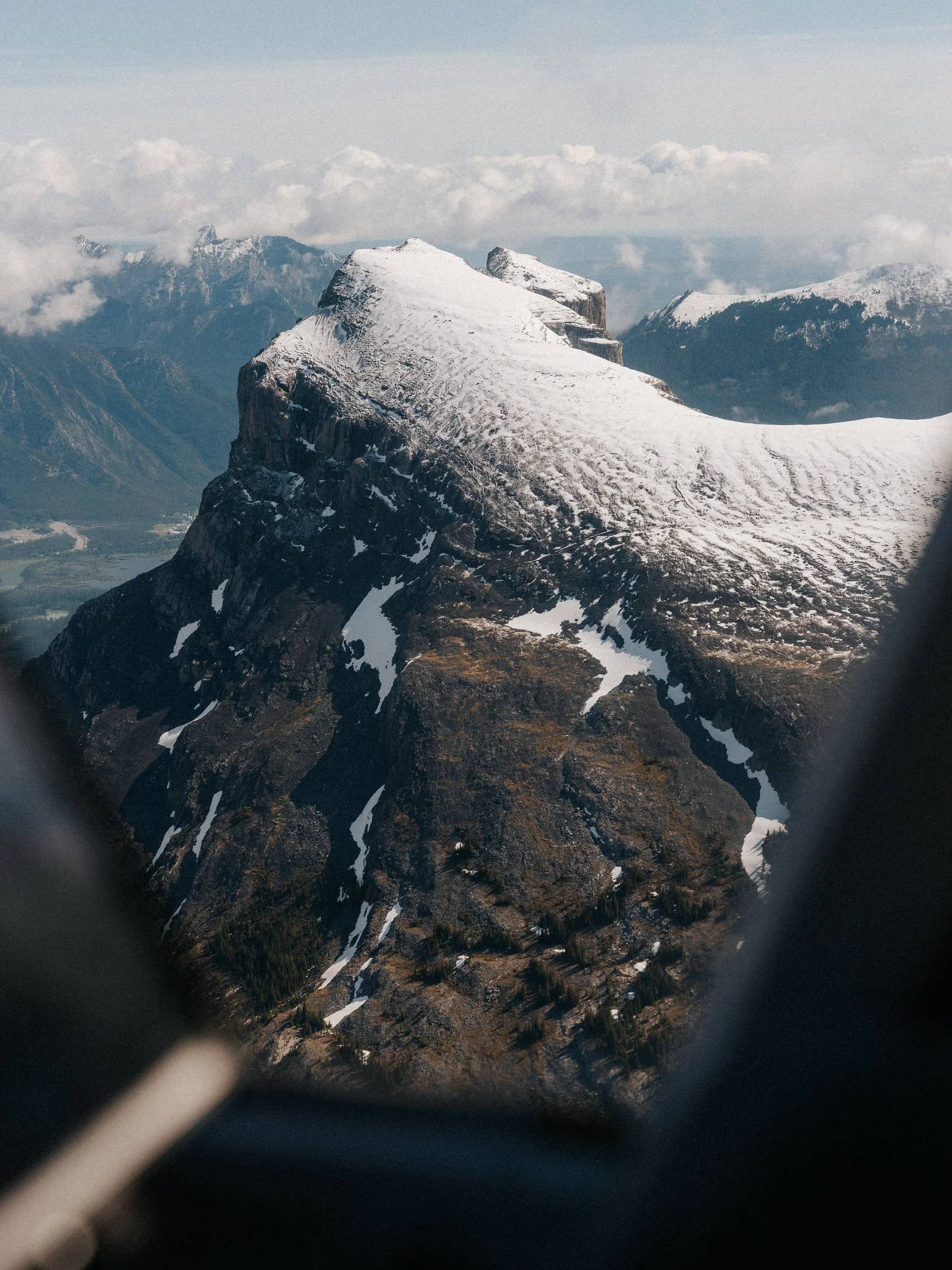 Snow-capped mountain peaks viewed through airplane window, with blurred window frame edges.
