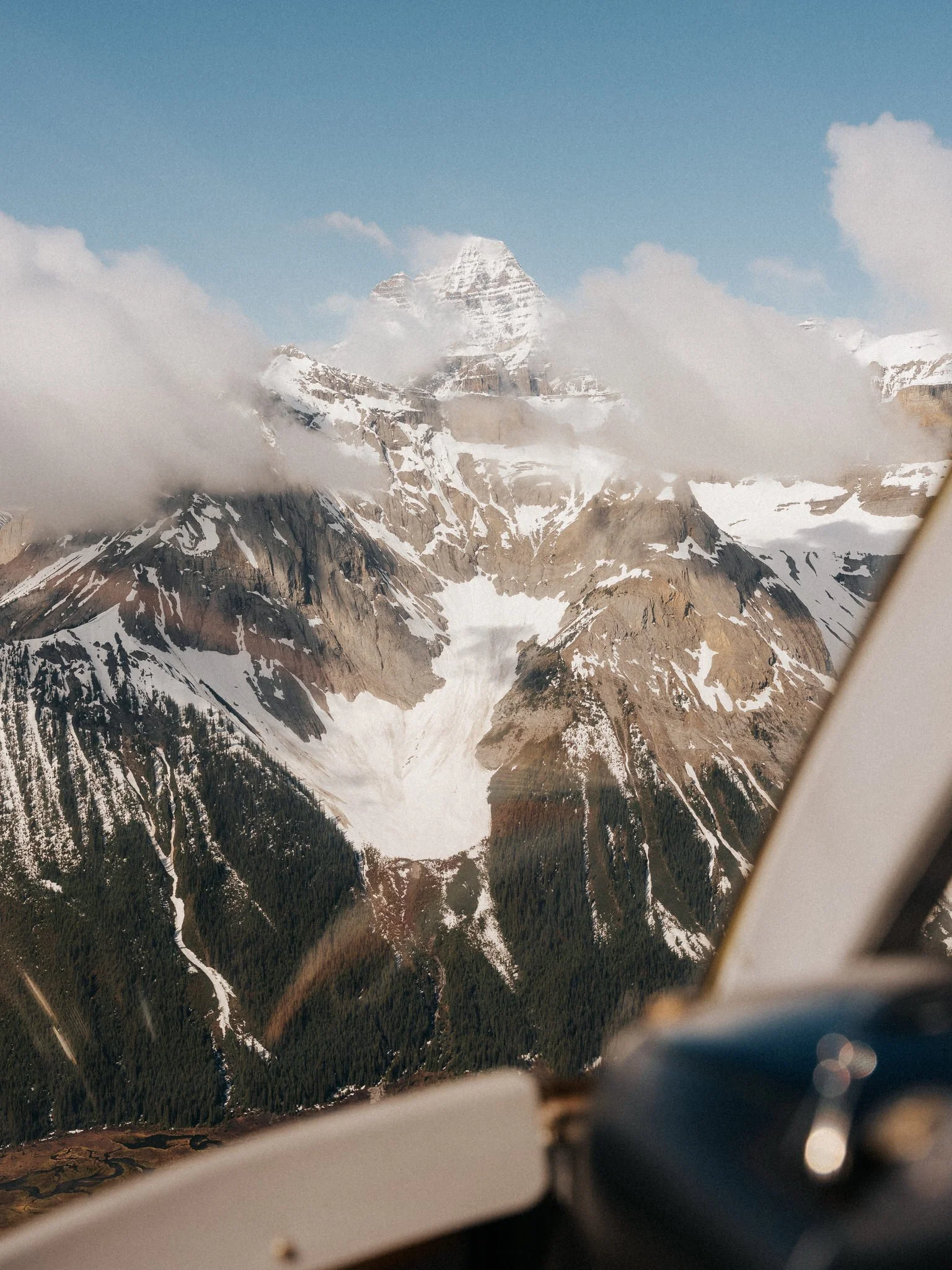 Snow-capped mountain peaks partially obscured by clouds, seen from an airplane window.