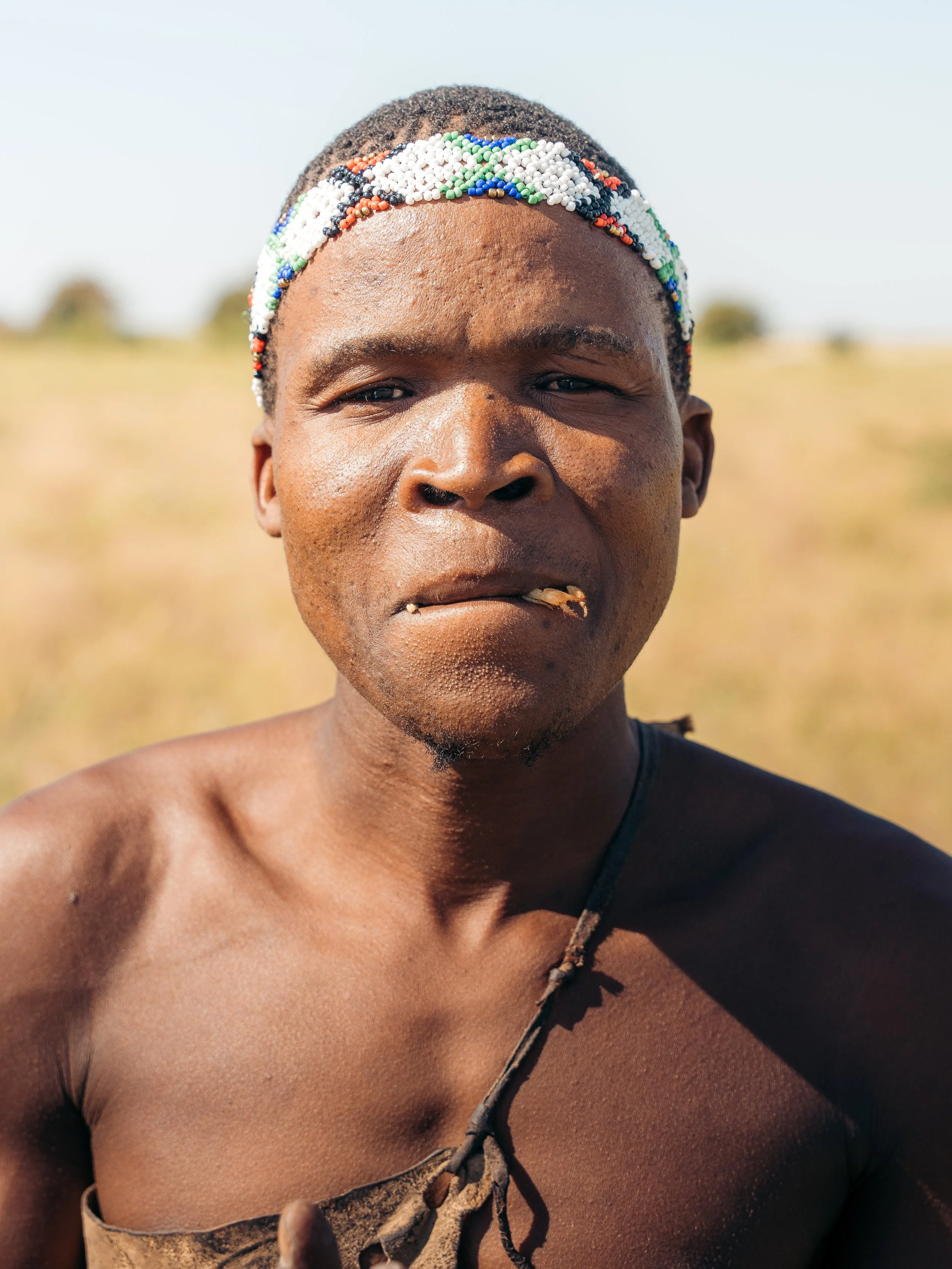 Close-up of a person wearing a beaded headband outdoors with a blurry background of a grassy plain and trees.