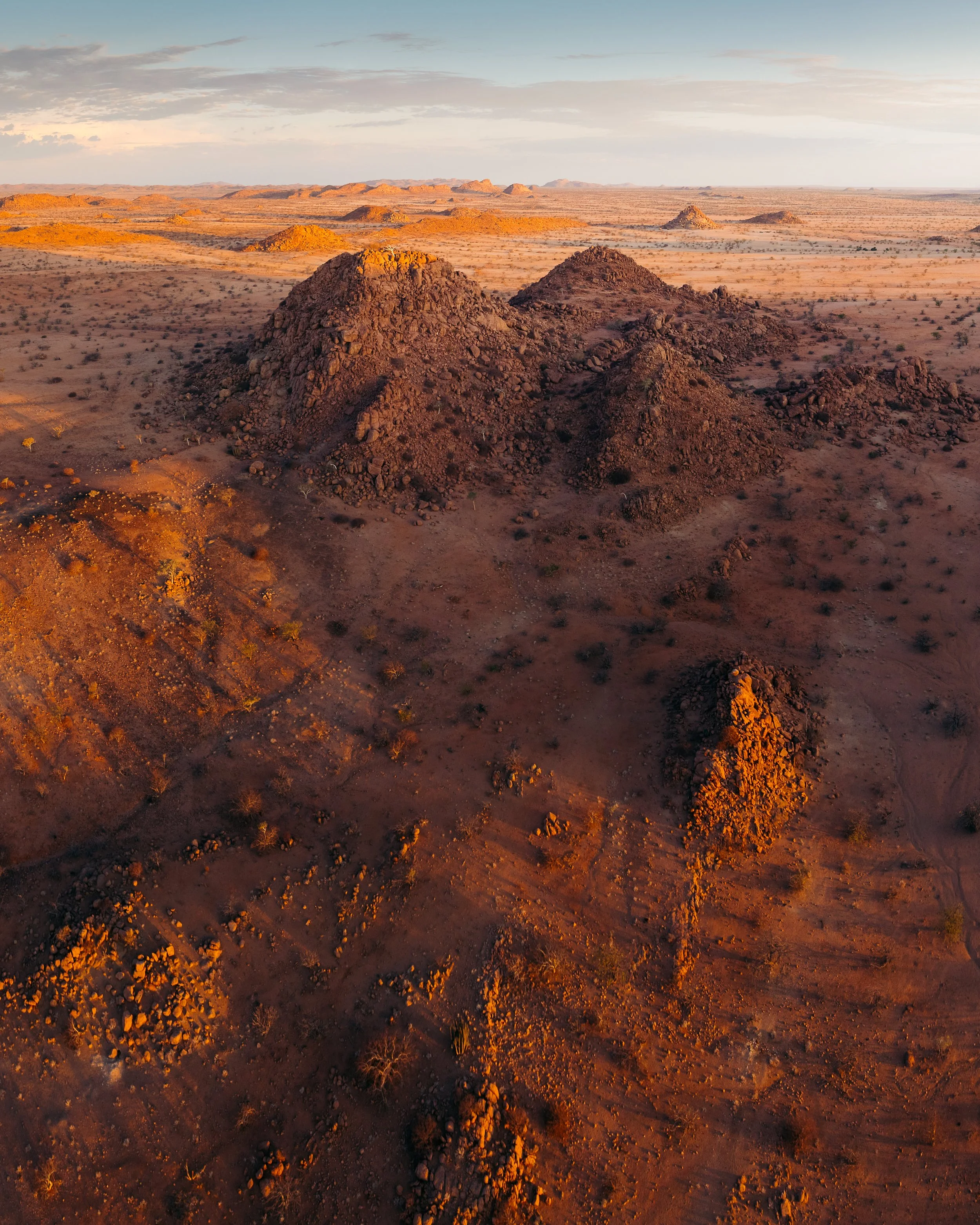 Aerial view of a desert landscape with rocky hills and sparse vegetation at sunset.