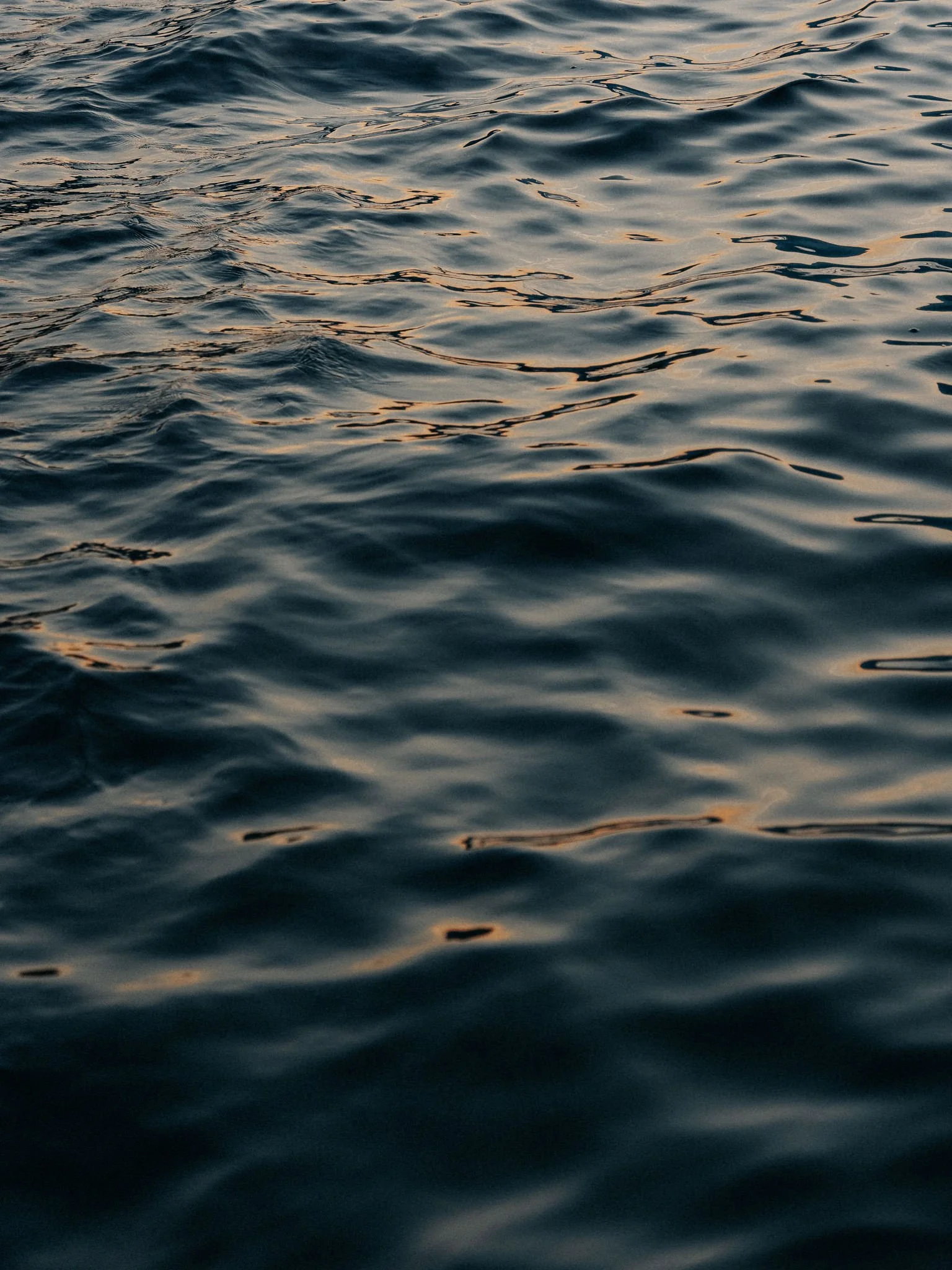 Calm water with gentle ripples and reflections of the sky, possibly at sunset or sunrise.