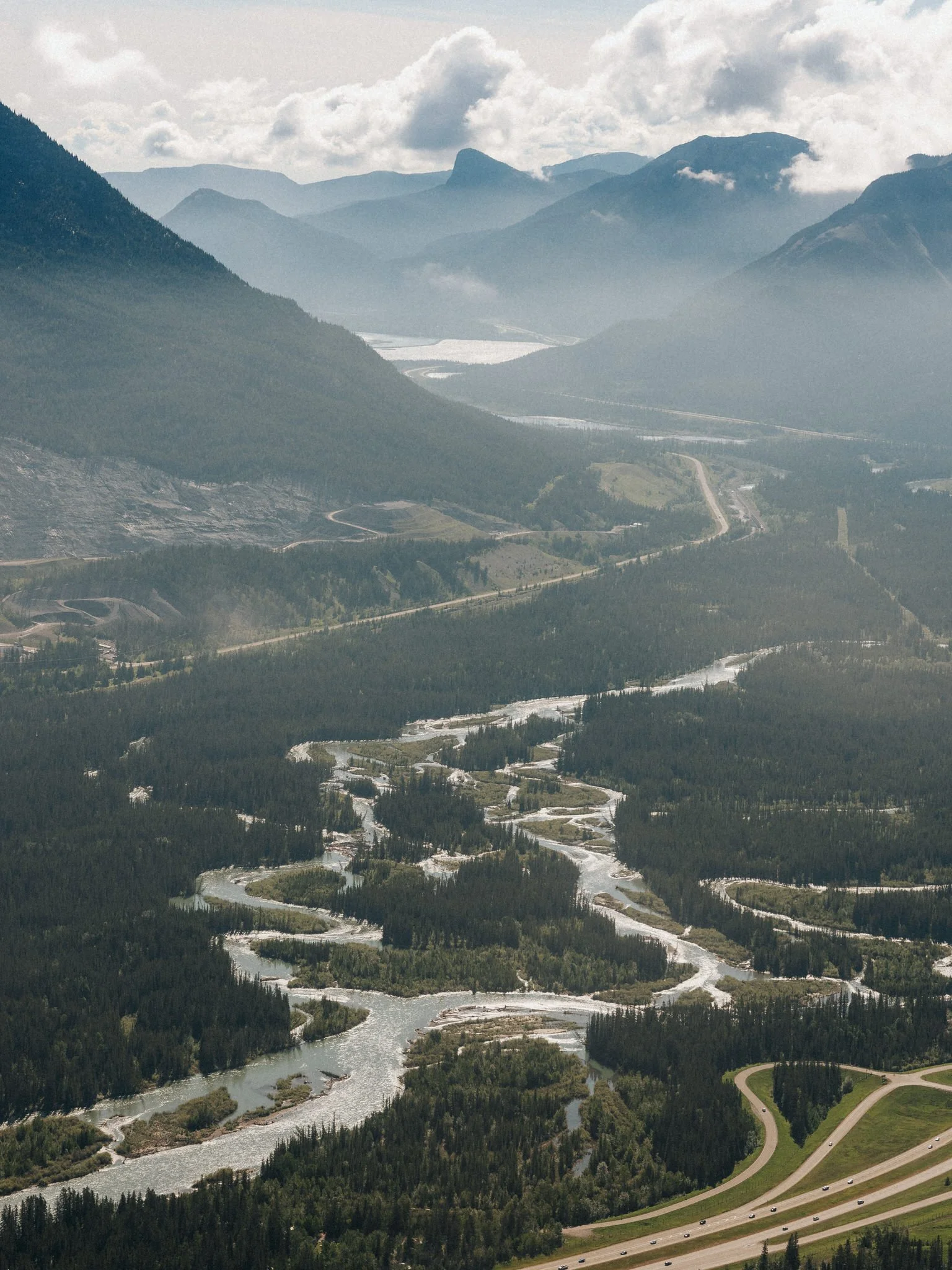 Aerial view of a winding river flowing through a forested mountain landscape with a highway running alongside.