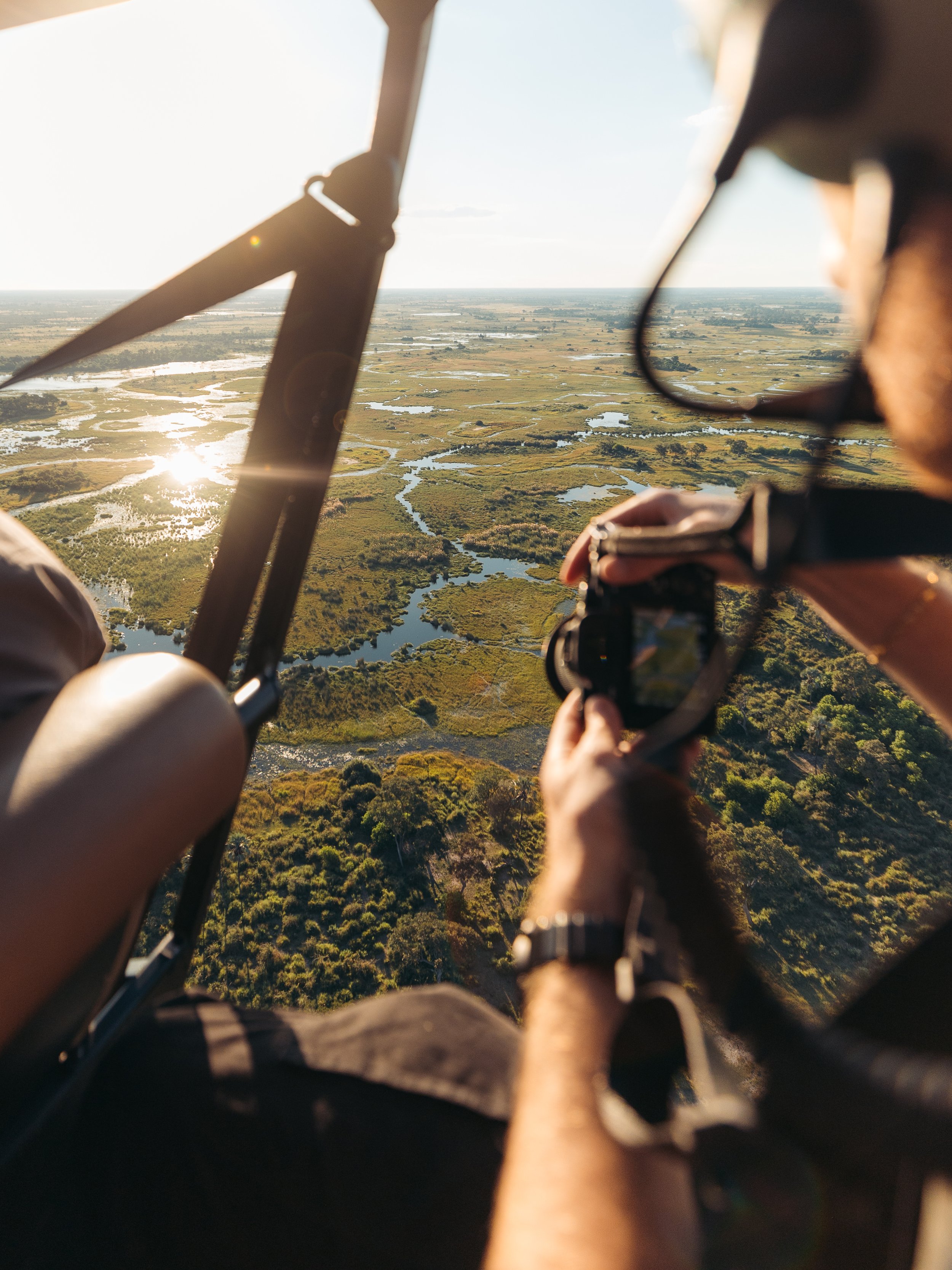 Aerial view from a helicopter showing wetlands, water channels, and vegetation during sunset.