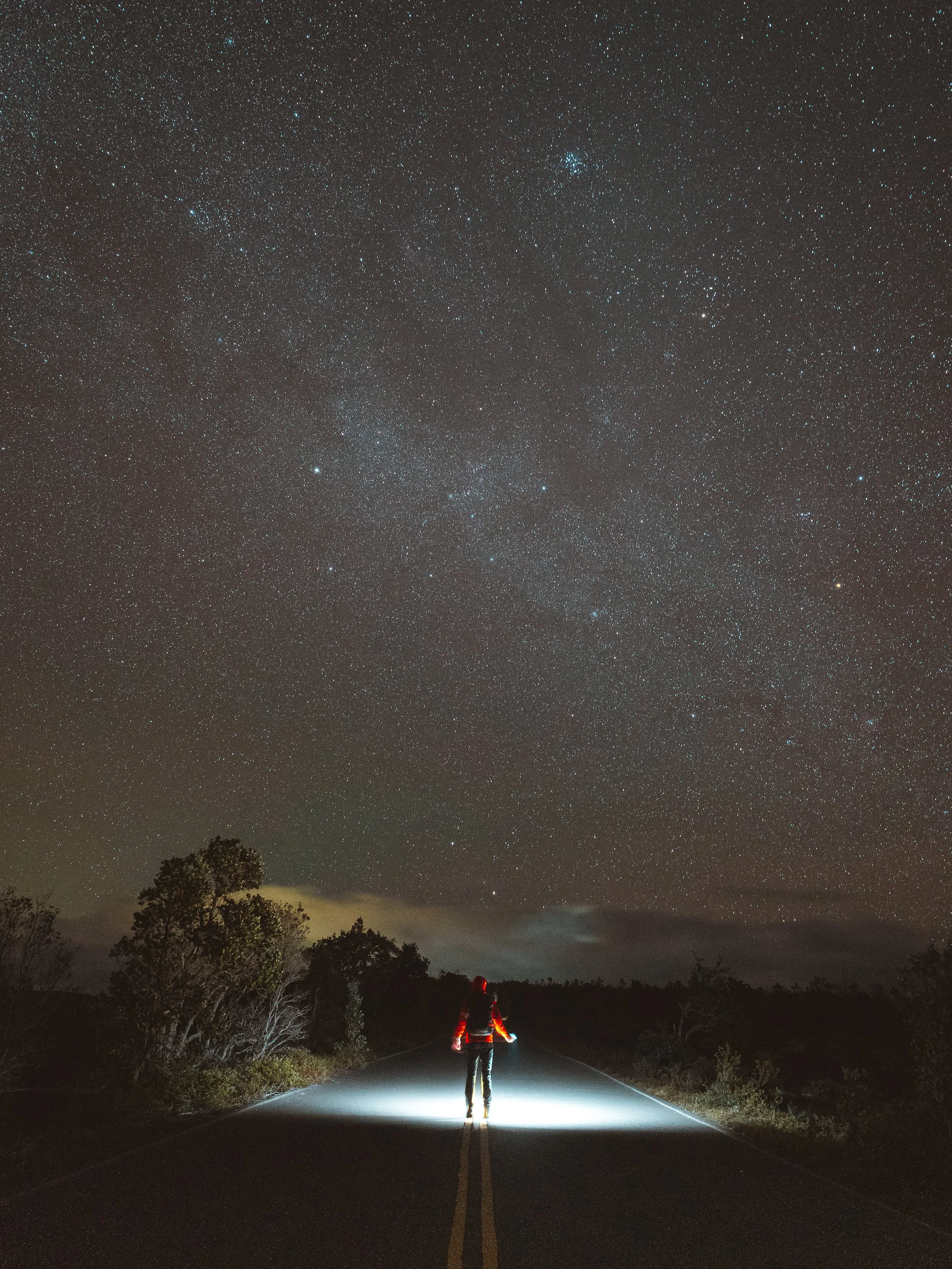 A person walking alone on a deserted road at night under a sky filled with stars.