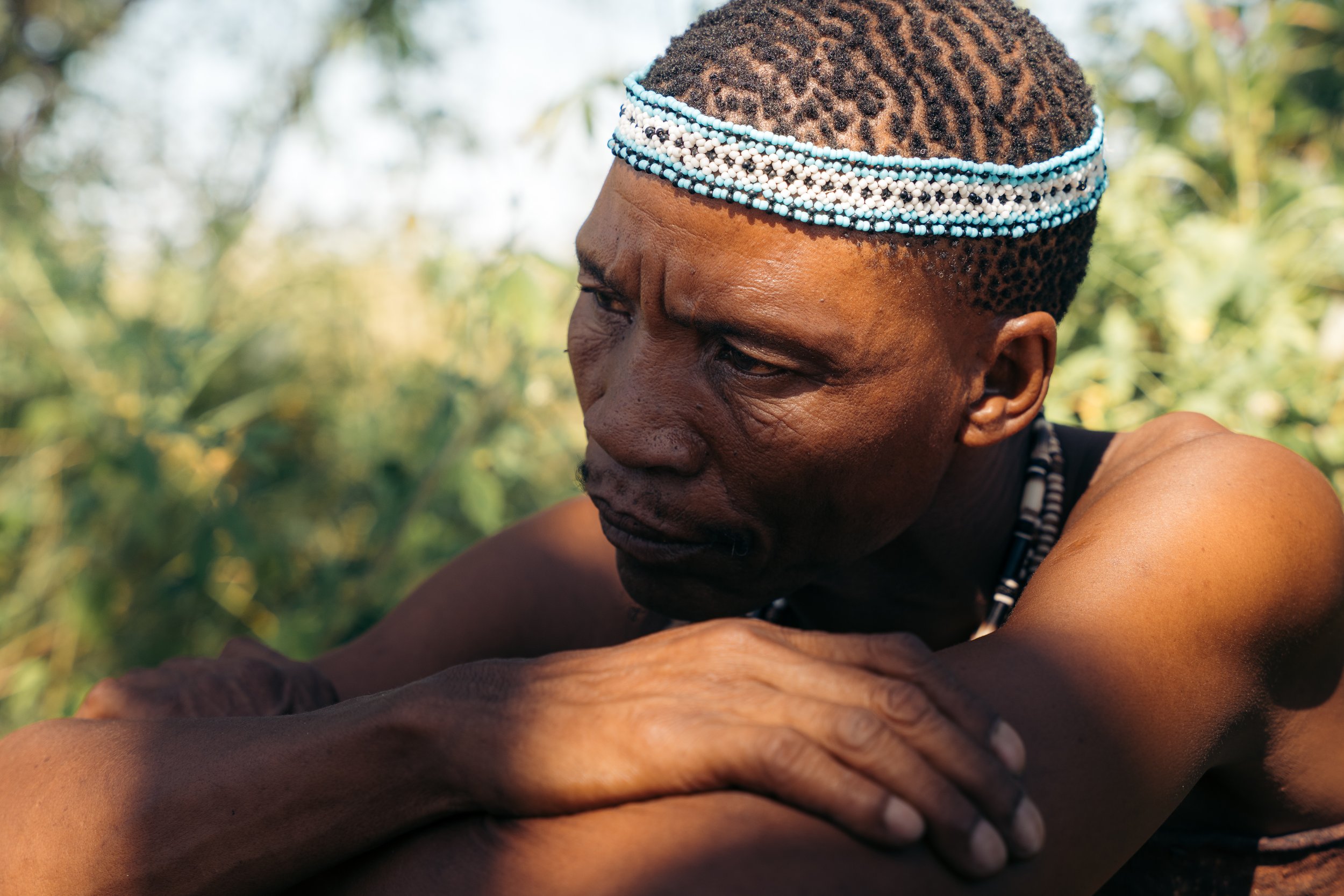 Close-up of an Indigenous person with traditional beaded headwear and jewelry, outdoors in natural light.