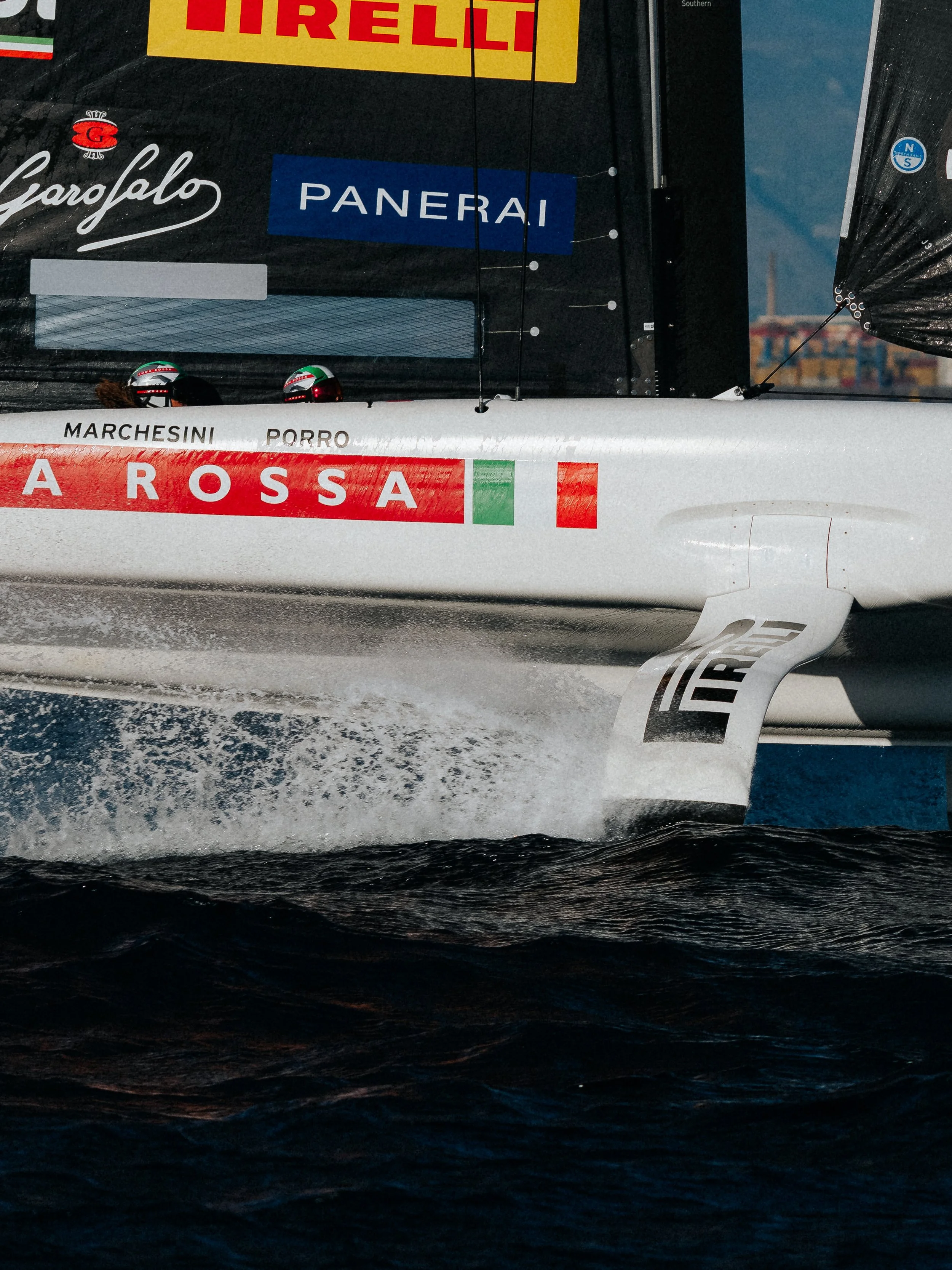 A racing boat on water with visible sponsor logos, including 'A ROSS A', 'PANERAI', and 'Pirelli', and helmets on the boat deck.
