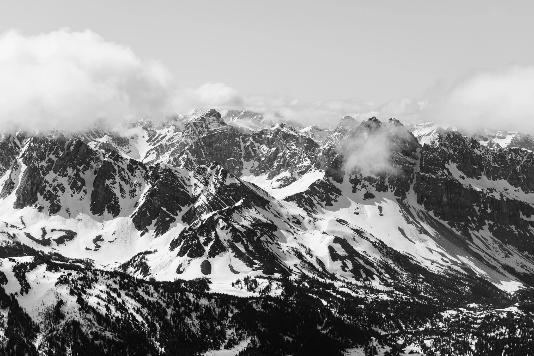 Snow-covered mountain range with rugged peaks and clouds overhead.
