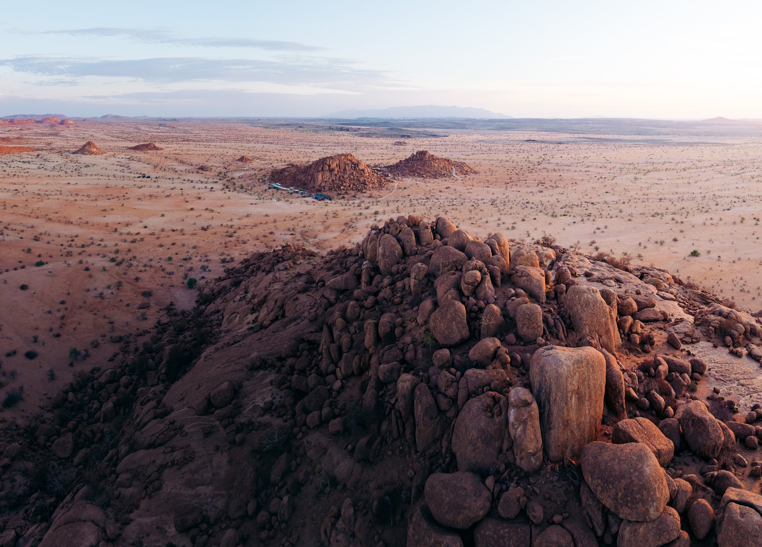 Aerial view of a desert landscape with large rock formations and sparse vegetation, under a partly cloudy sky.