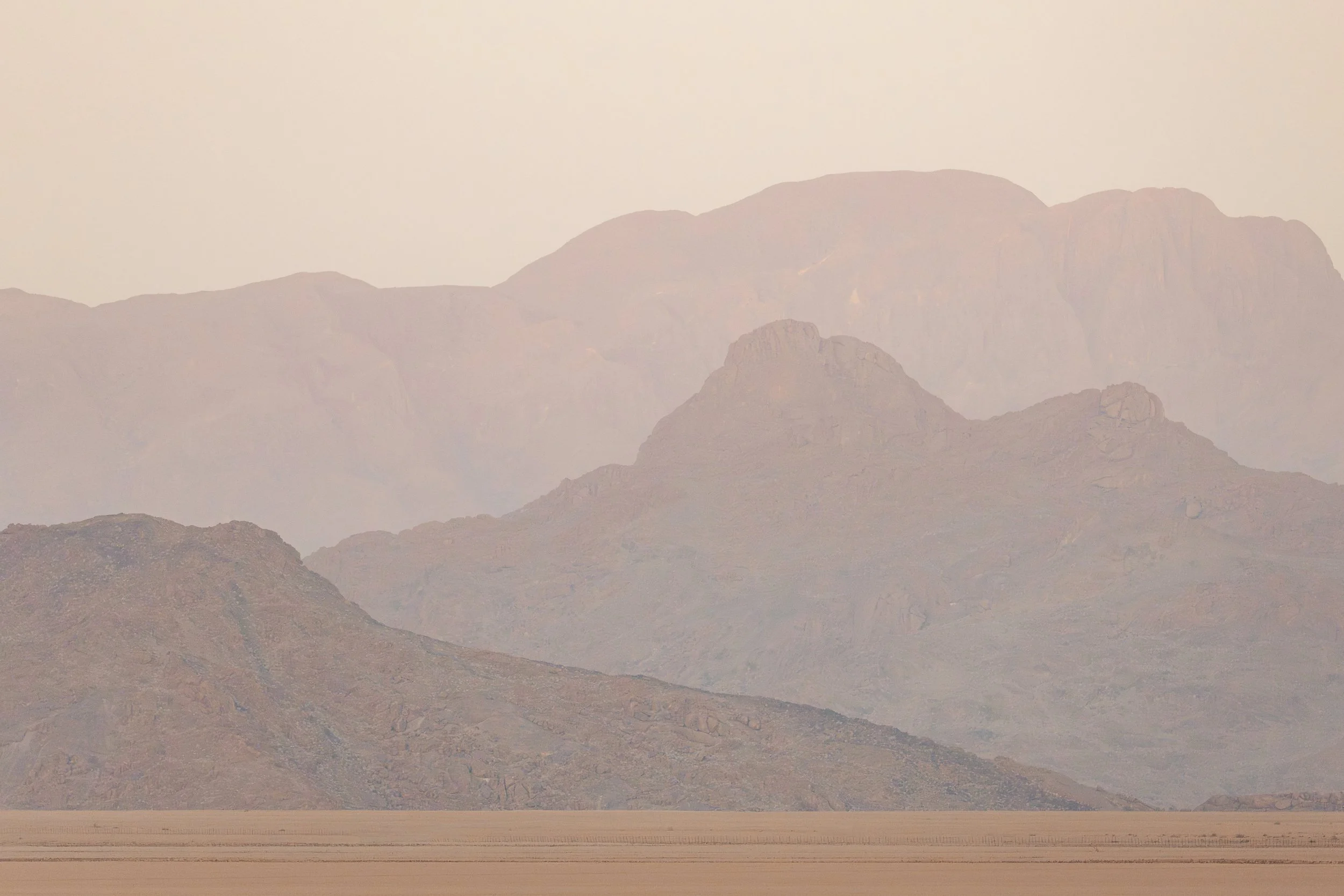 A barren desert landscape with mountains in the background, under a hazy sky.