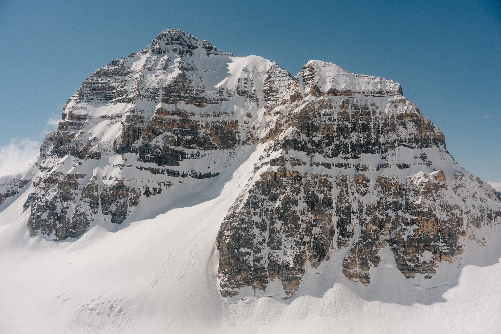 Snow-covered mountain peak with rugged rock faces and a clear blue sky in the background.